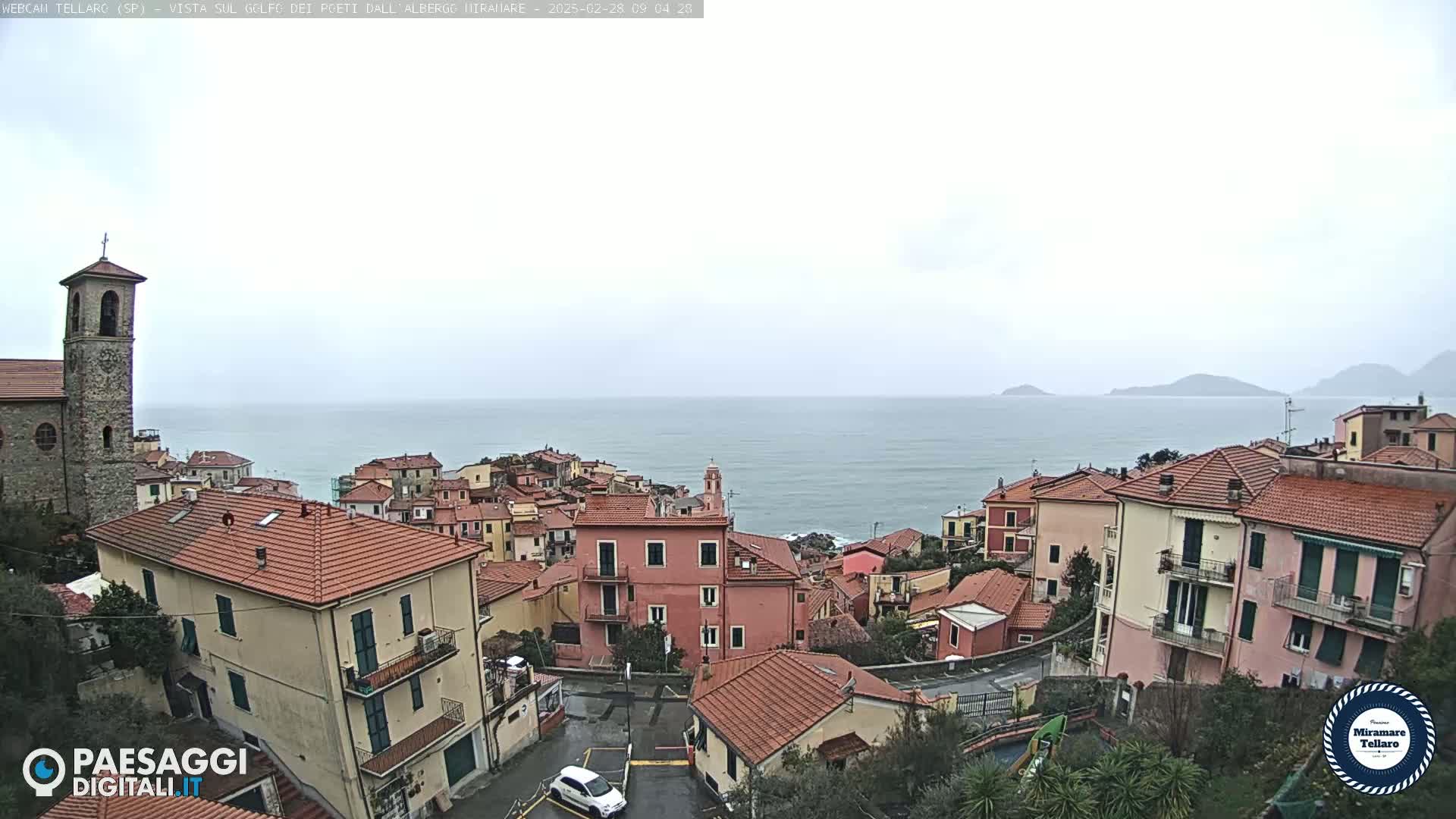A coastal town with red-tiled roofs overlooks a calm sea under an overcast sky.
