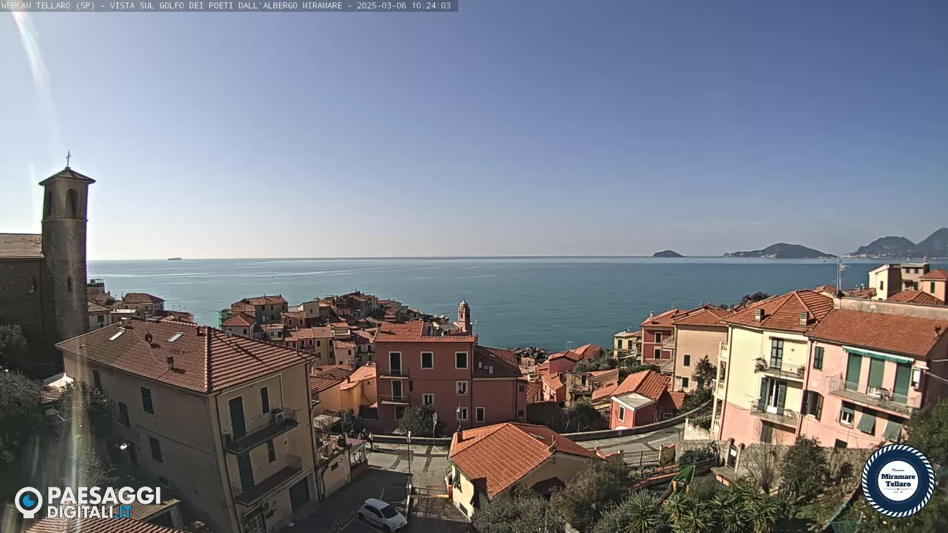 A coastal town with red-tiled roofs overlooks a calm blue sea under a clear sky.