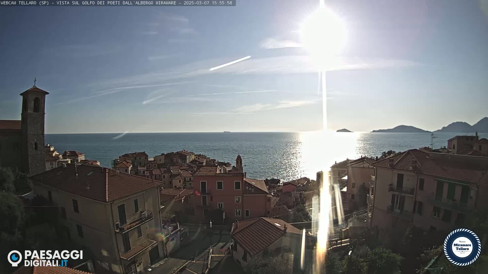 A coastal town with red-tiled roofs overlooks a sunlit sea under a mostly clear sky.
