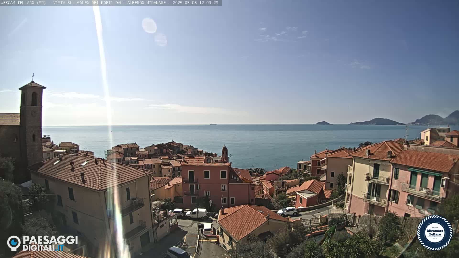 A coastal town with red-tiled roofs overlooks a calm sea under a clear, sunny sky.