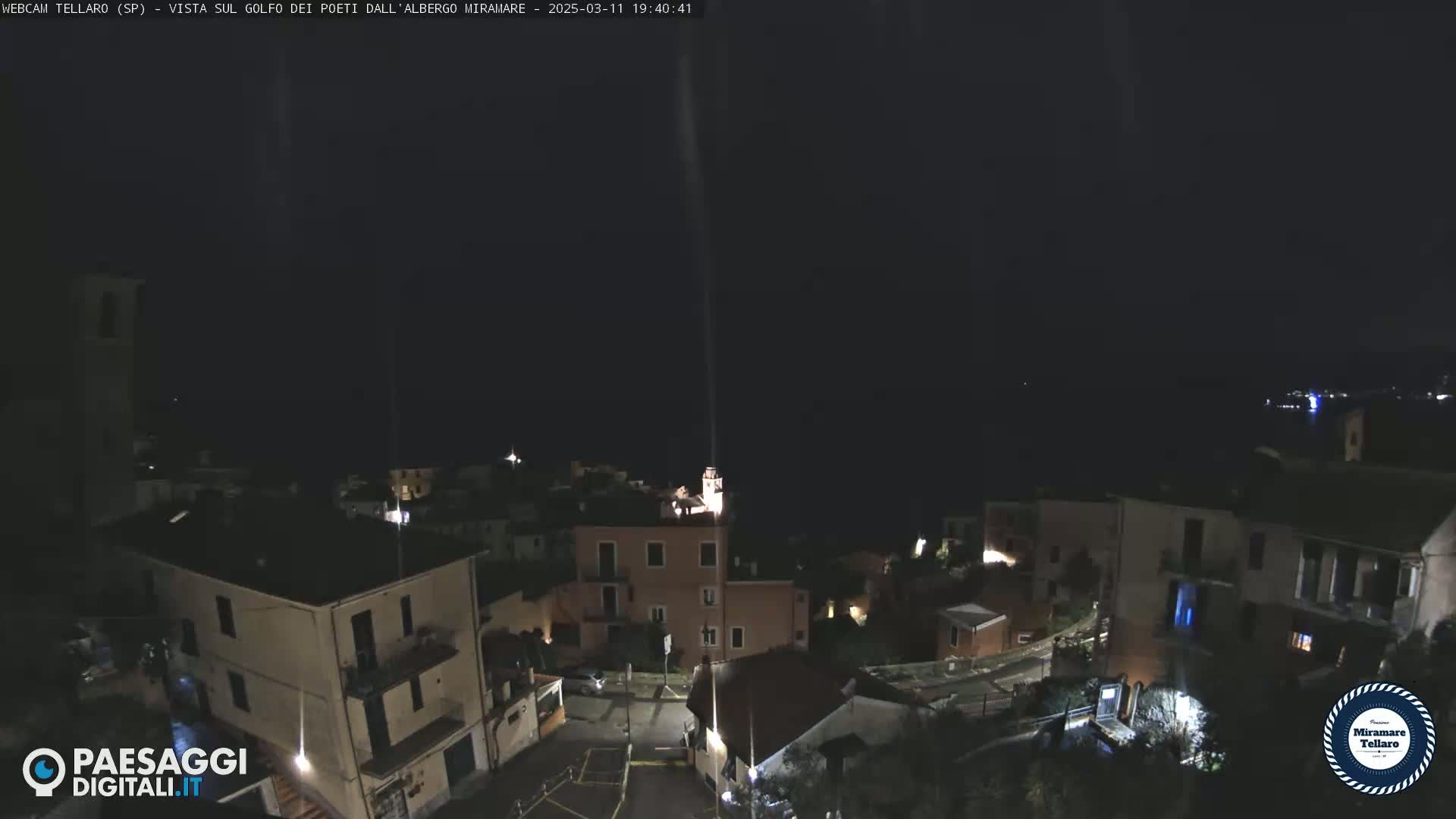 A nighttime, high-angle view of a coastal town with buildings illuminated against a dark sky.
