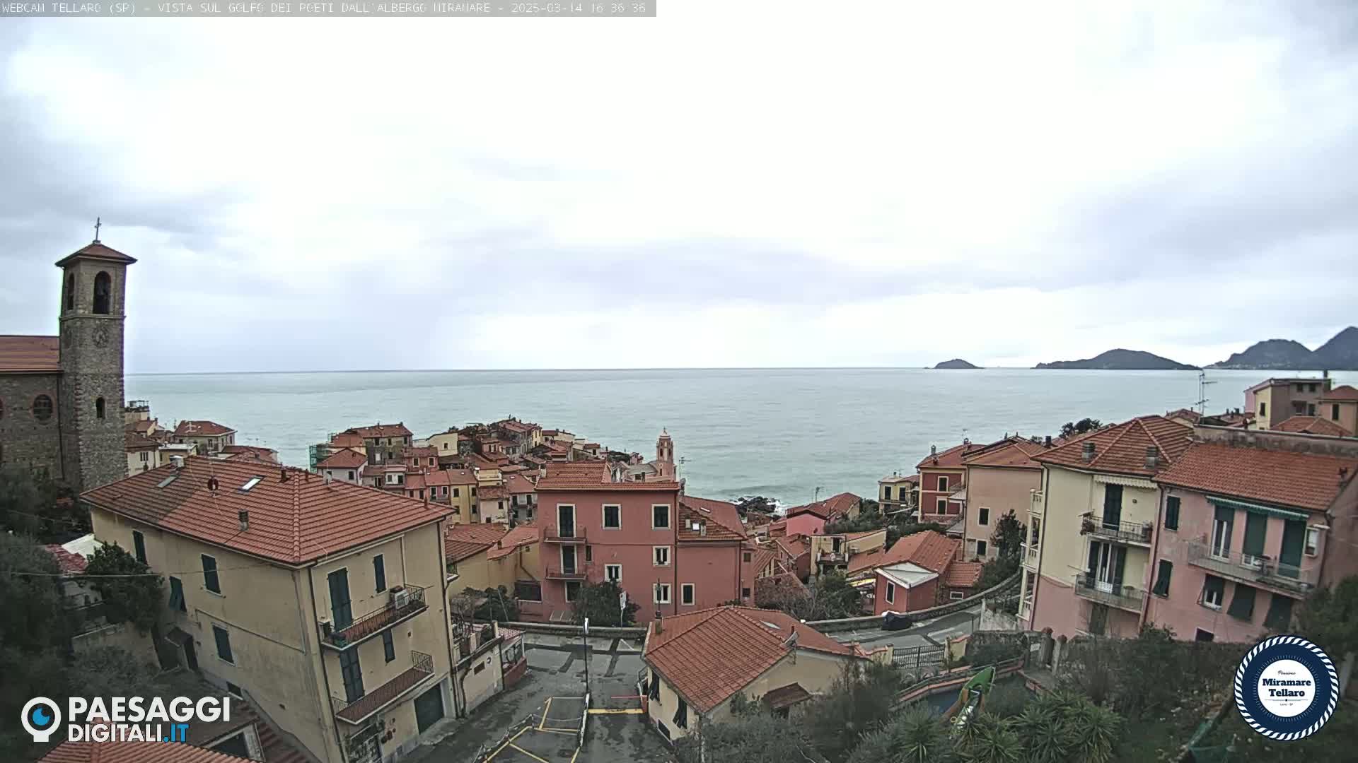 A coastal town with red-tiled roofs overlooks a calm sea under an overcast sky.