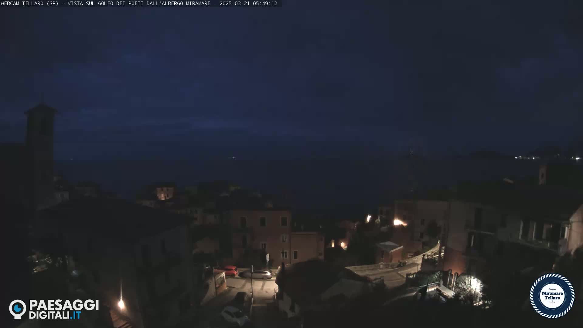A dark, nighttime view of a coastal town overlooking a calm, dark sea.