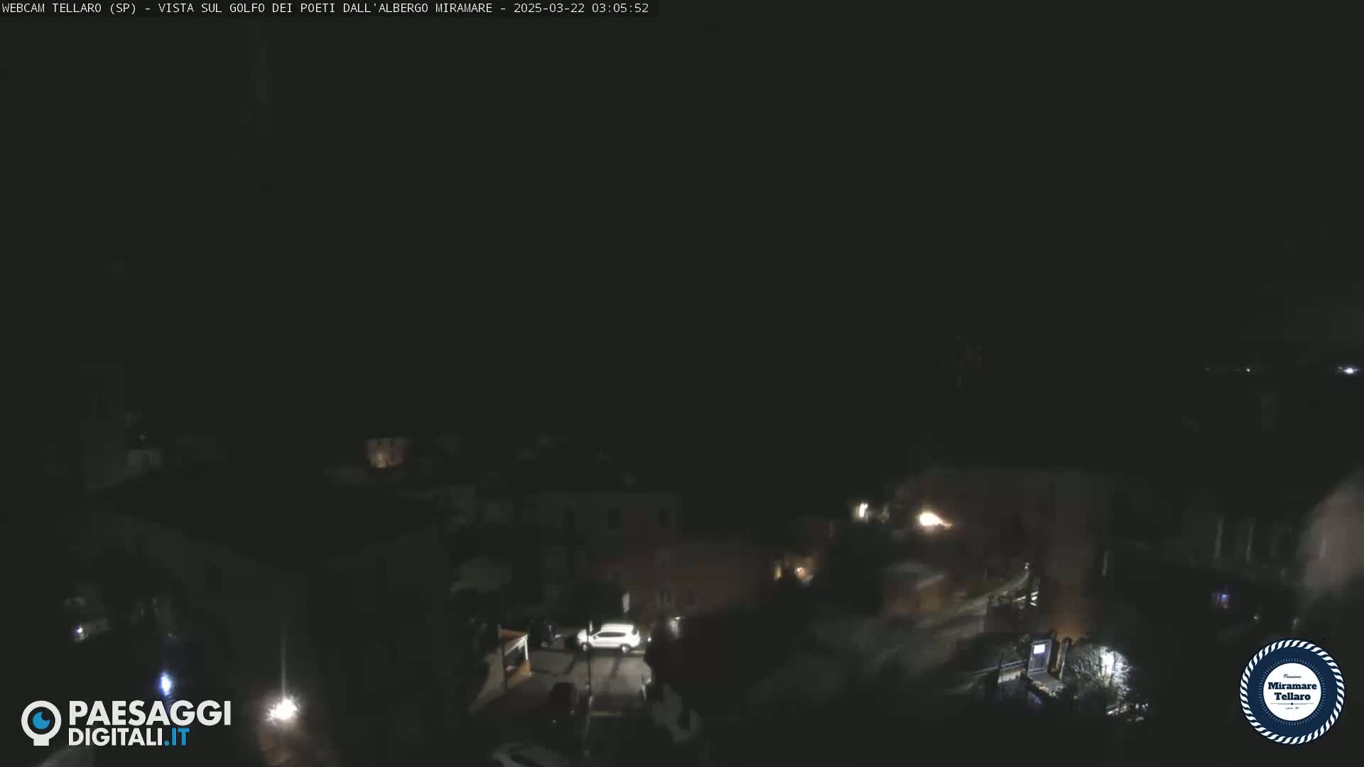 A nighttime, dark view of a town with a few dimly lit buildings and vehicles.