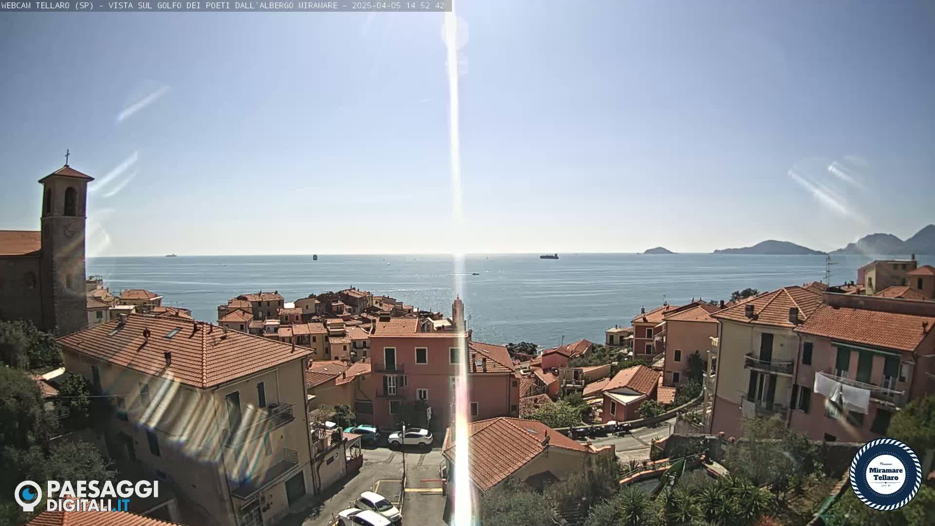 A coastal town with red-tiled roofs overlooks a calm sea under a sunny sky.