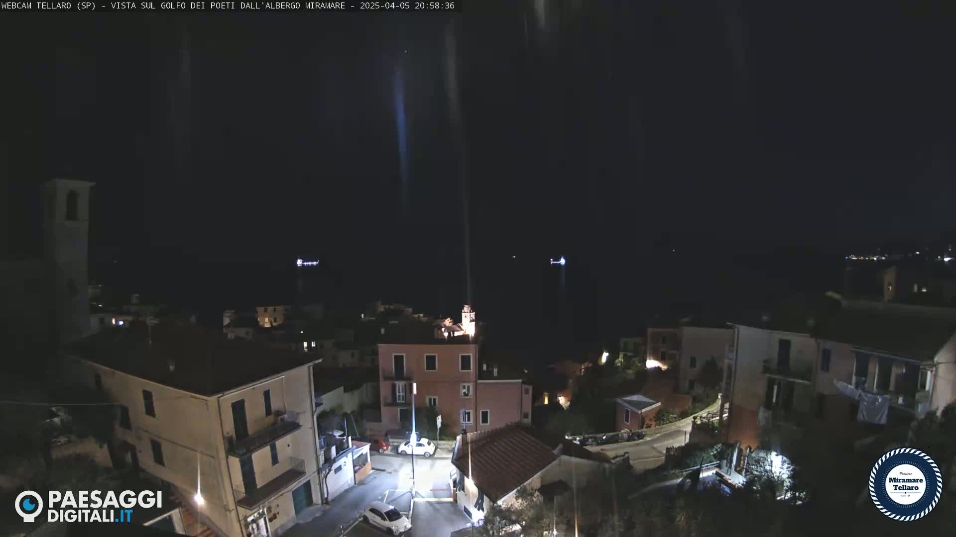A nighttime, aerial view of a coastal town with buildings illuminated against a dark sky and sea.