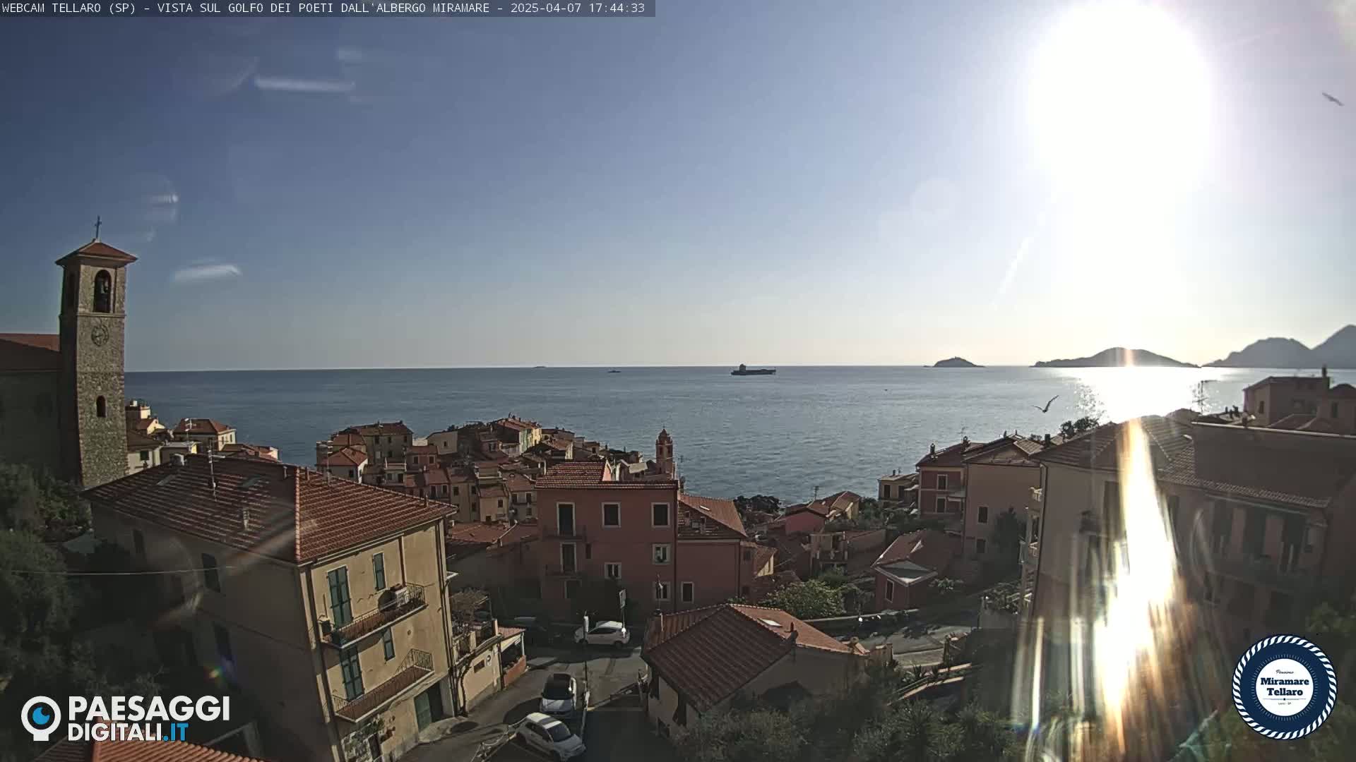 A sunlit coastal town overlooks a calm sea with distant islands under a clear sky.