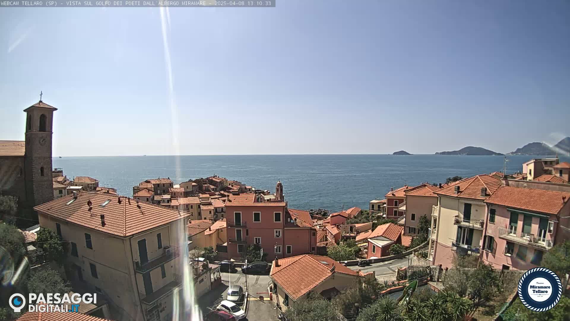 A coastal town with red-tiled roofs overlooks a calm blue sea under a clear sky.
