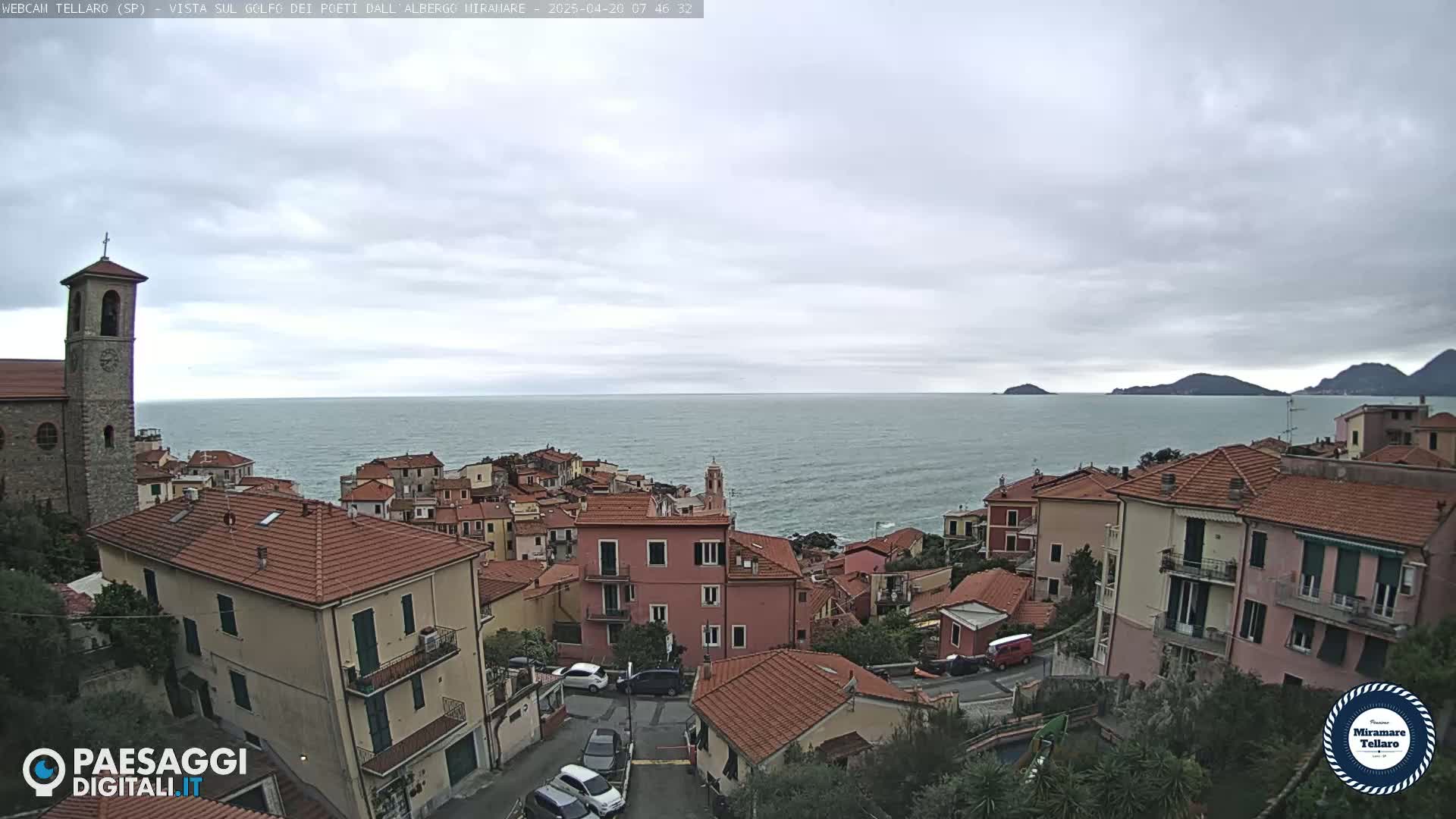 A coastal town with red-tiled roofs overlooks a calm sea under an overcast sky.