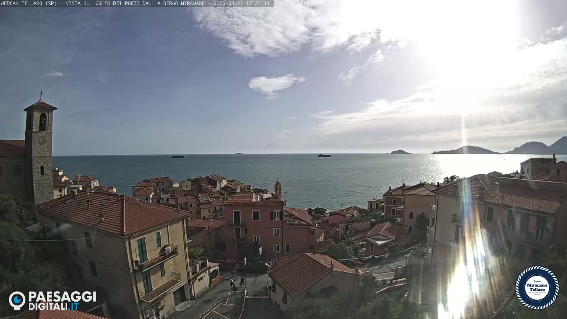 A coastal town with red-tiled roofs overlooks a calm sea under a partly cloudy sky.