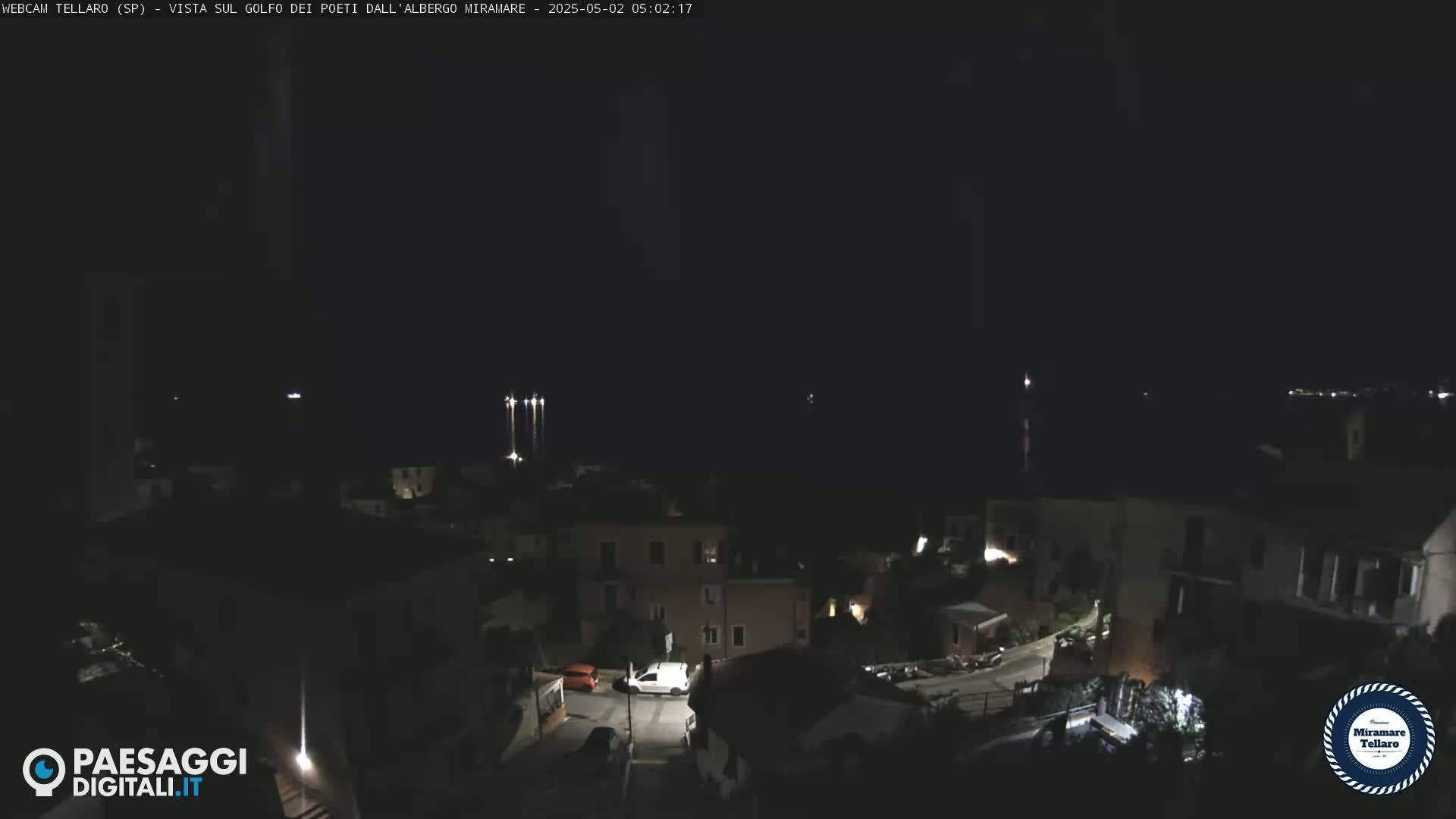 A nighttime view of a coastal town with dimly lit buildings and streets, overlooking a dark body of water.
