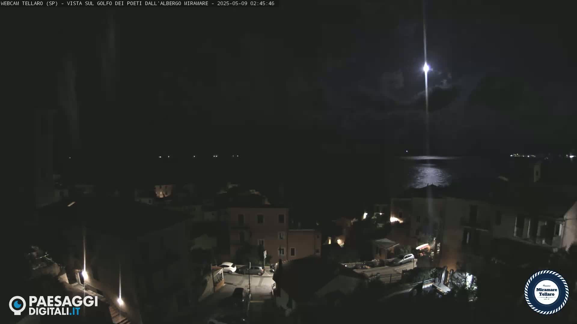 A nighttime view of a coastal town with a bright light shining over the dark water.
