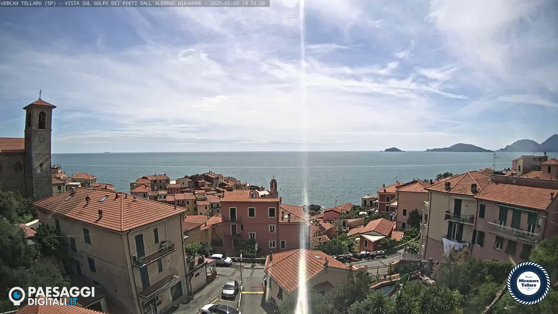 A coastal town with red-tiled roofs overlooks a calm sea under a partly cloudy sky.