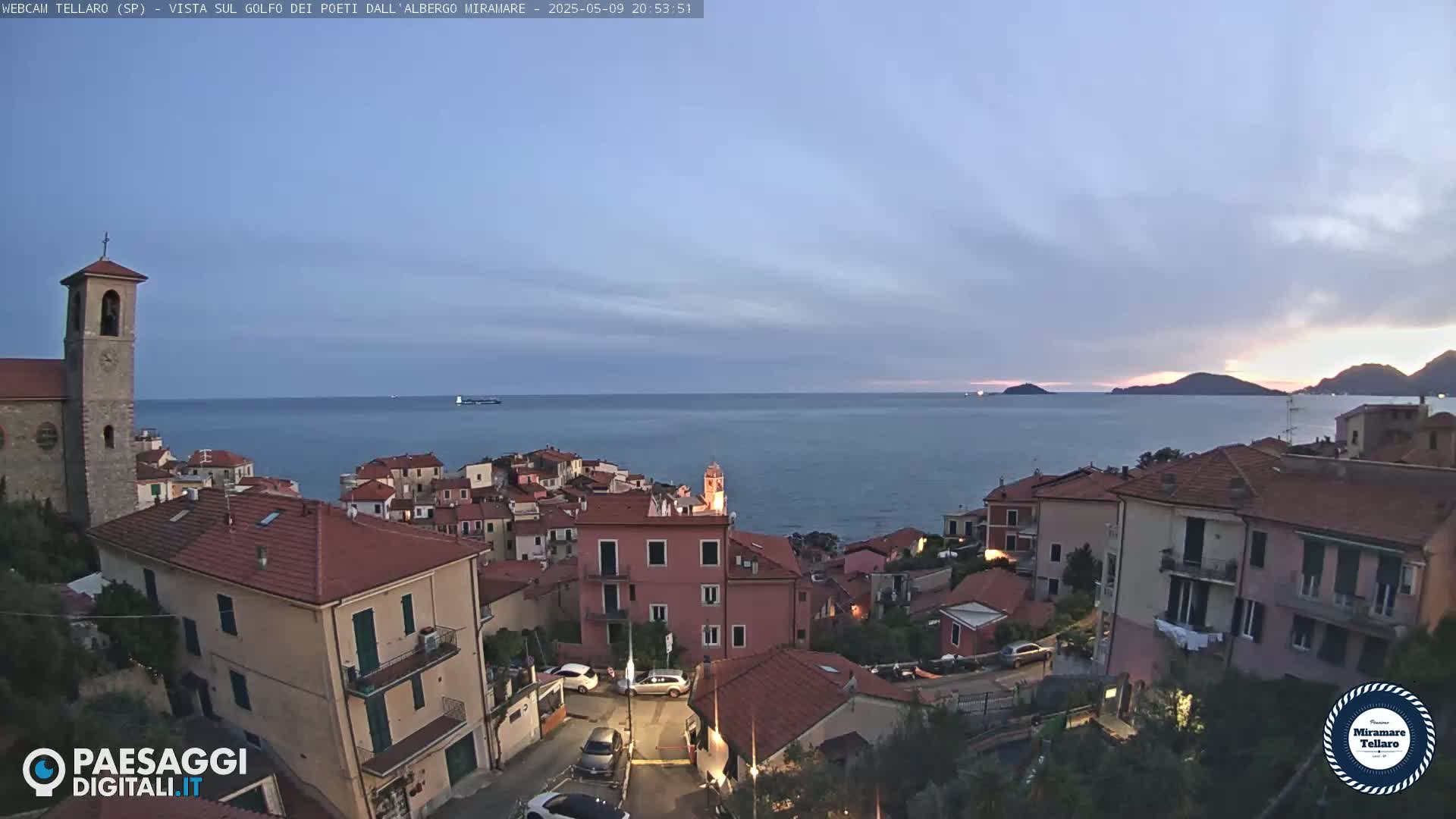 A coastal town with red-tiled roofs overlooks a calm sea under a twilight sky.
