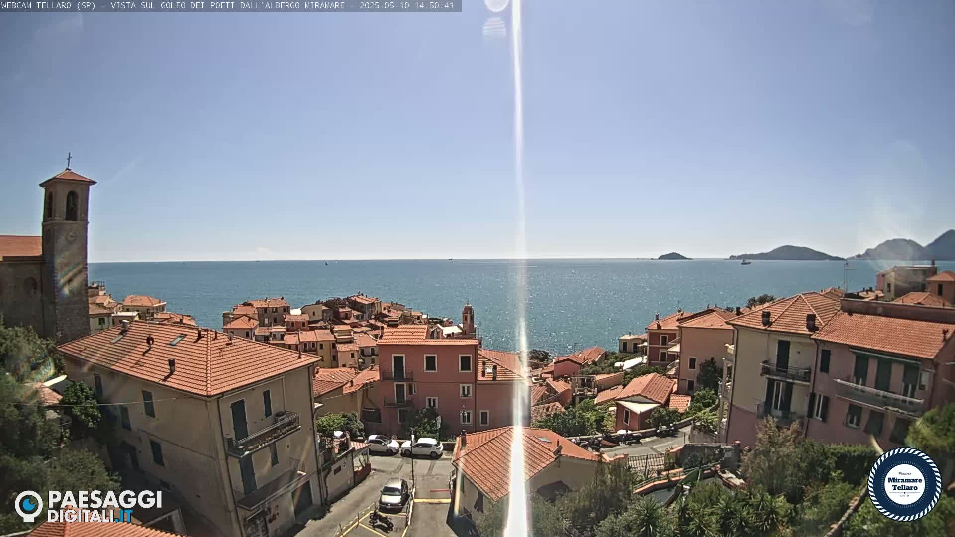A coastal town with red-tiled roofs overlooks a calm blue sea under a clear, sunny sky.