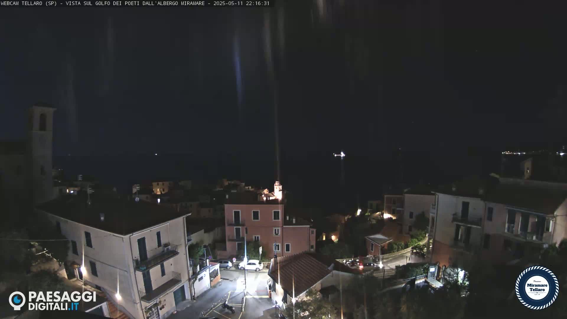 A nighttime view of a coastal town overlooking a dark body of water under a clear sky, with a few lights visible in the buildings.