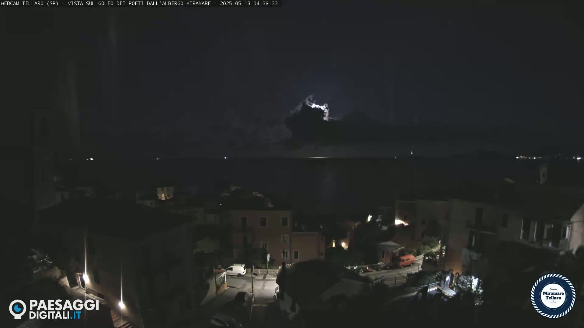 A nighttime view of a coastal town overlooking a dark sea under a stormy sky with lightning.