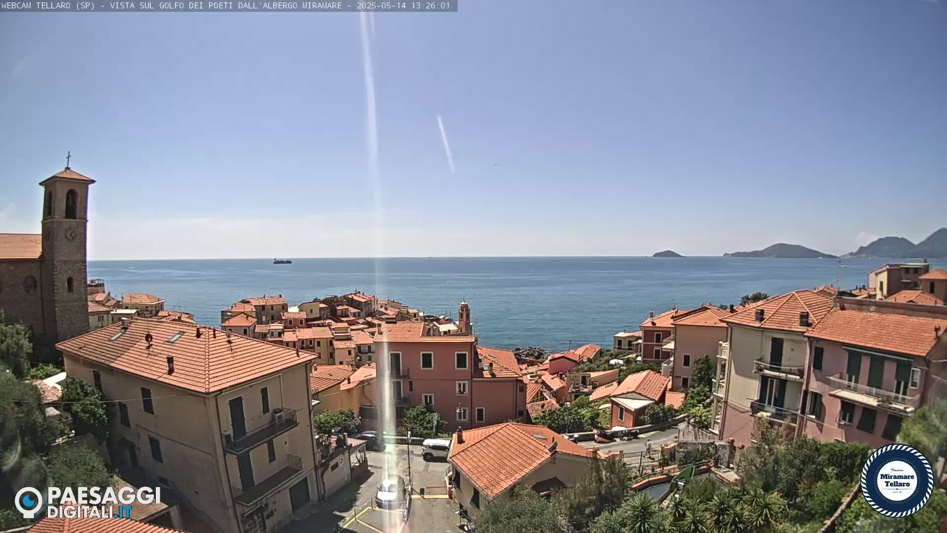 A coastal town with red-tiled roofs overlooks a calm blue sea under a clear sky.