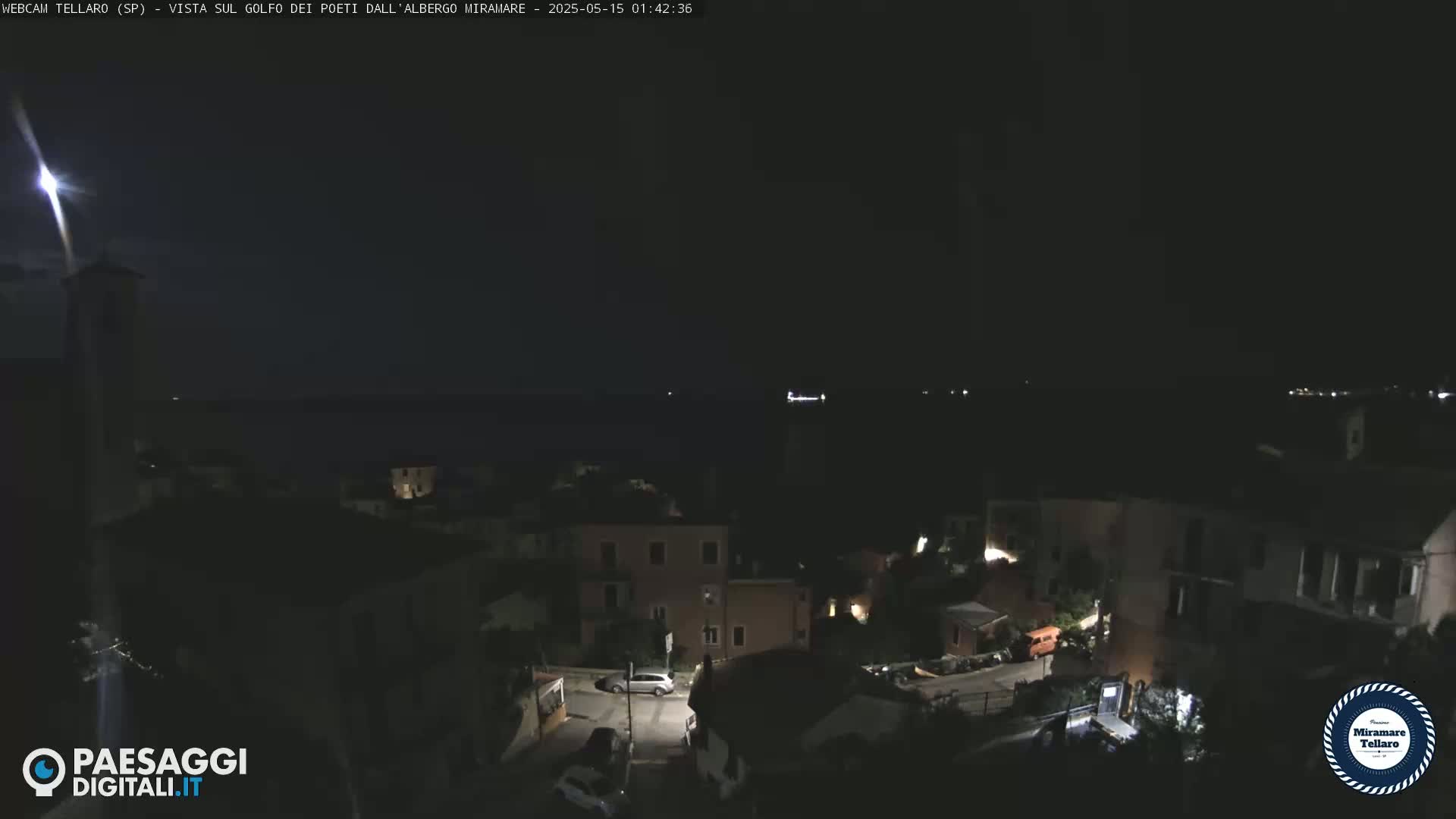 A nighttime view of a coastal town with dimly lit buildings and a dark body of water in the background under a clear sky.
