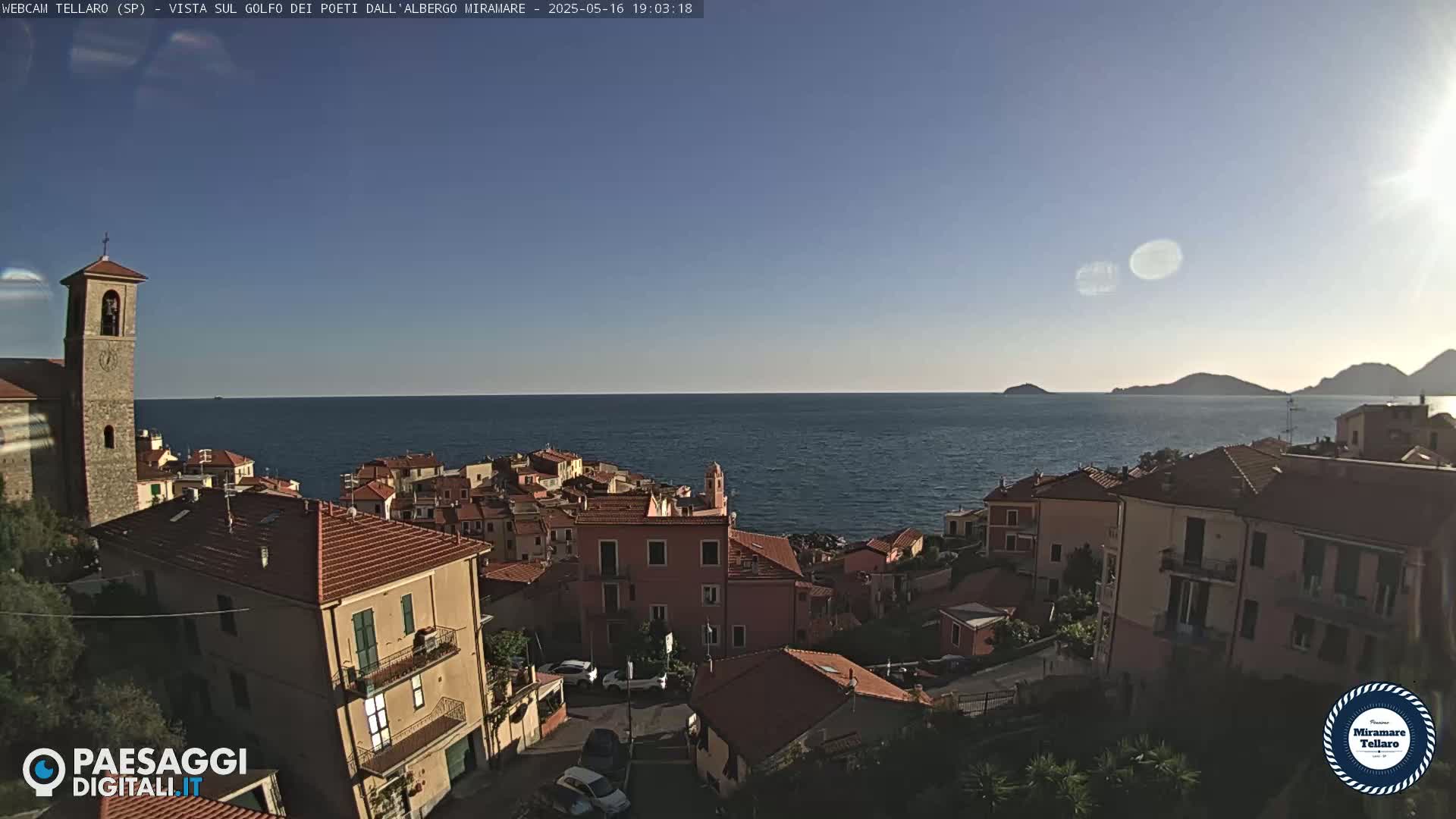 A coastal town with red-tiled roofs overlooks a calm blue sea under a clear, sunny sky.
