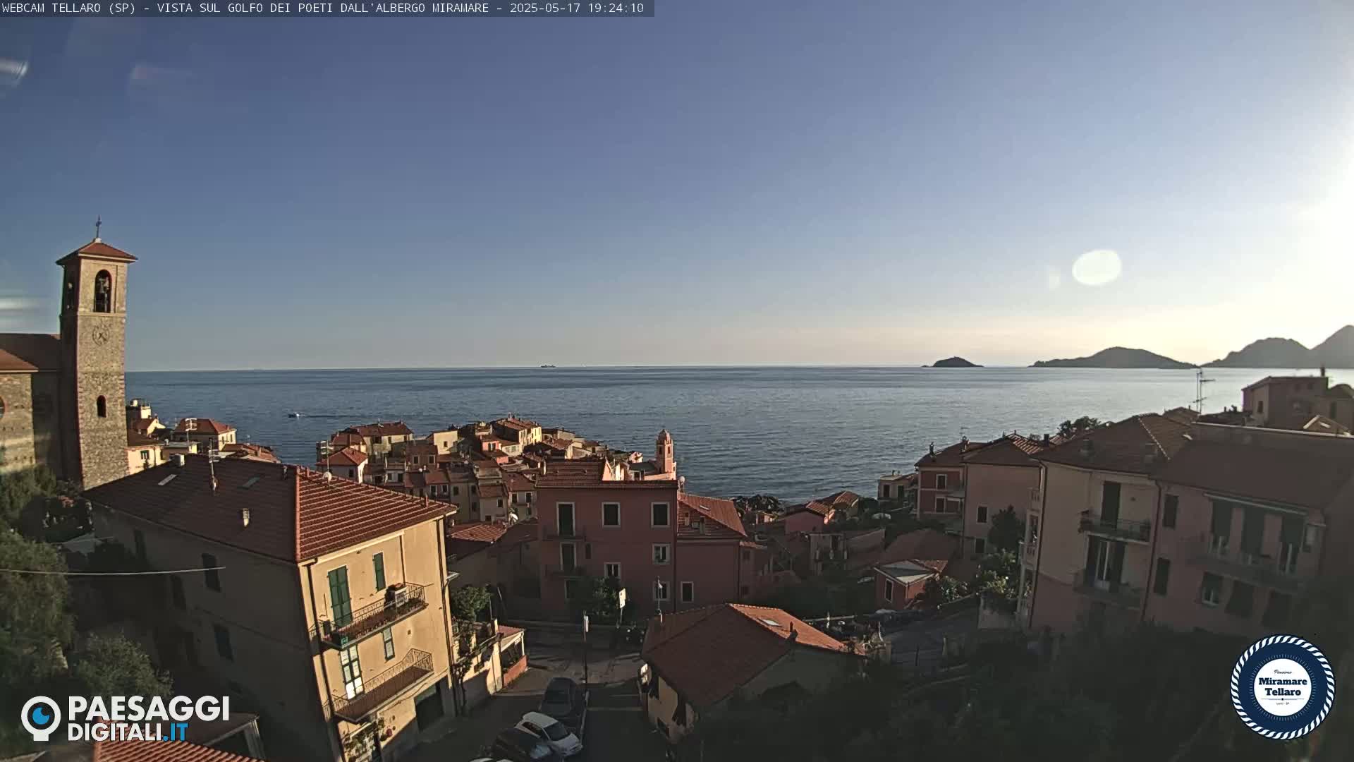 A coastal town with red-roofed buildings overlooks a calm sea under a clear, sunny sky.