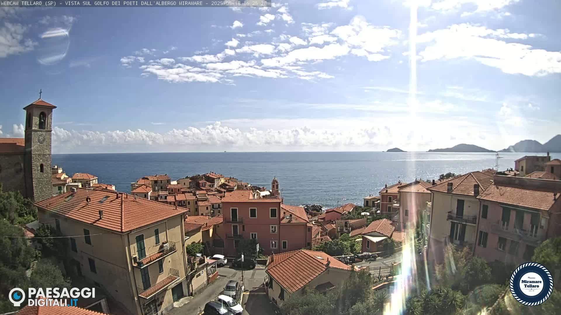 A coastal town with red-tiled roofs overlooks a calm ocean under a partly cloudy sky.