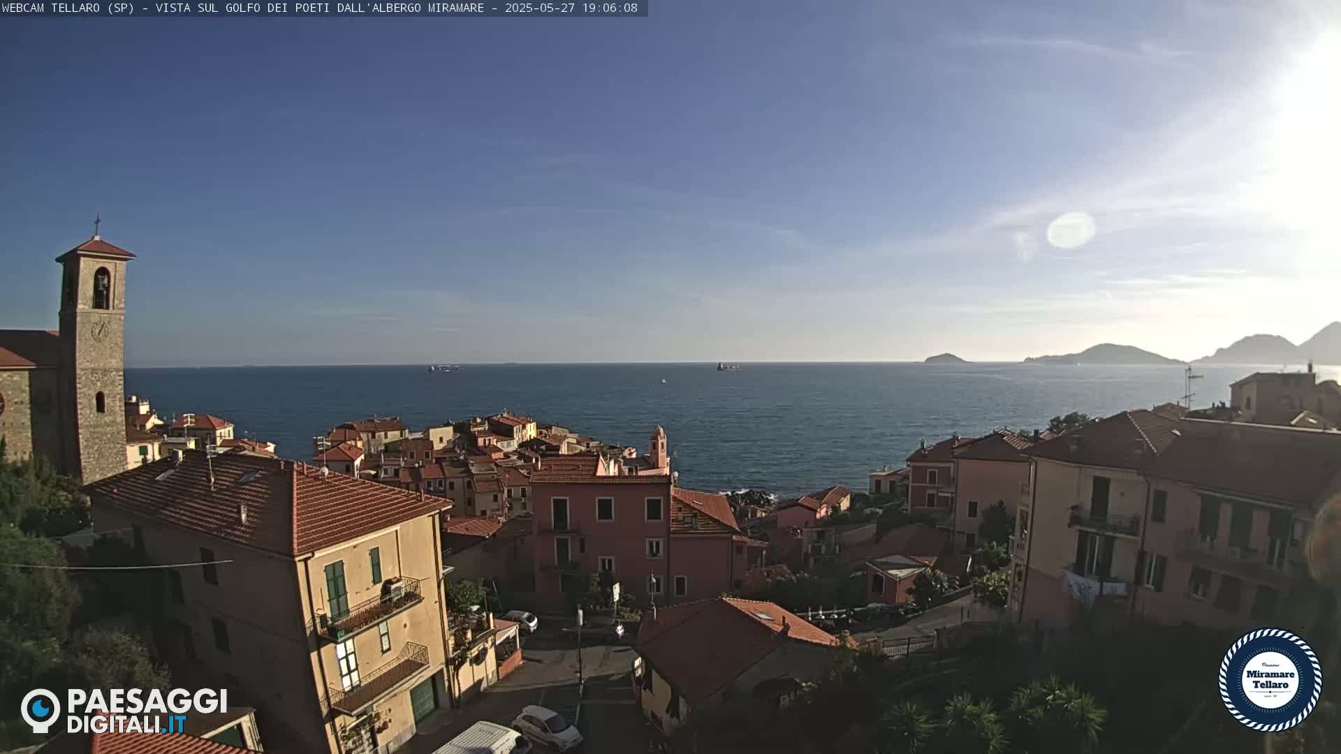 A coastal town with red-roofed buildings overlooks a calm sea under a clear, sunny sky.