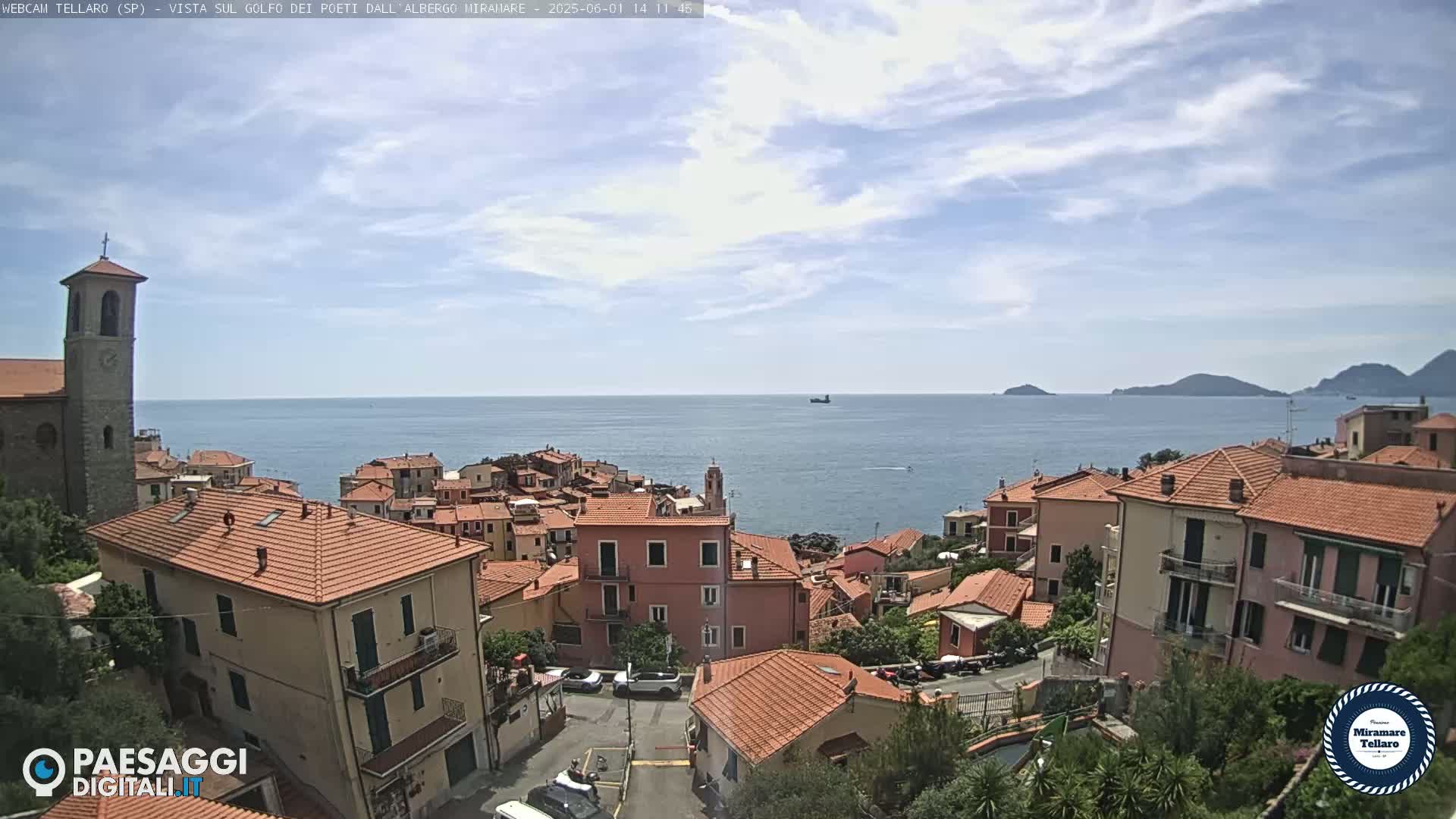 A coastal town with red-tiled roofs overlooks a calm sea under a partly cloudy sky.
