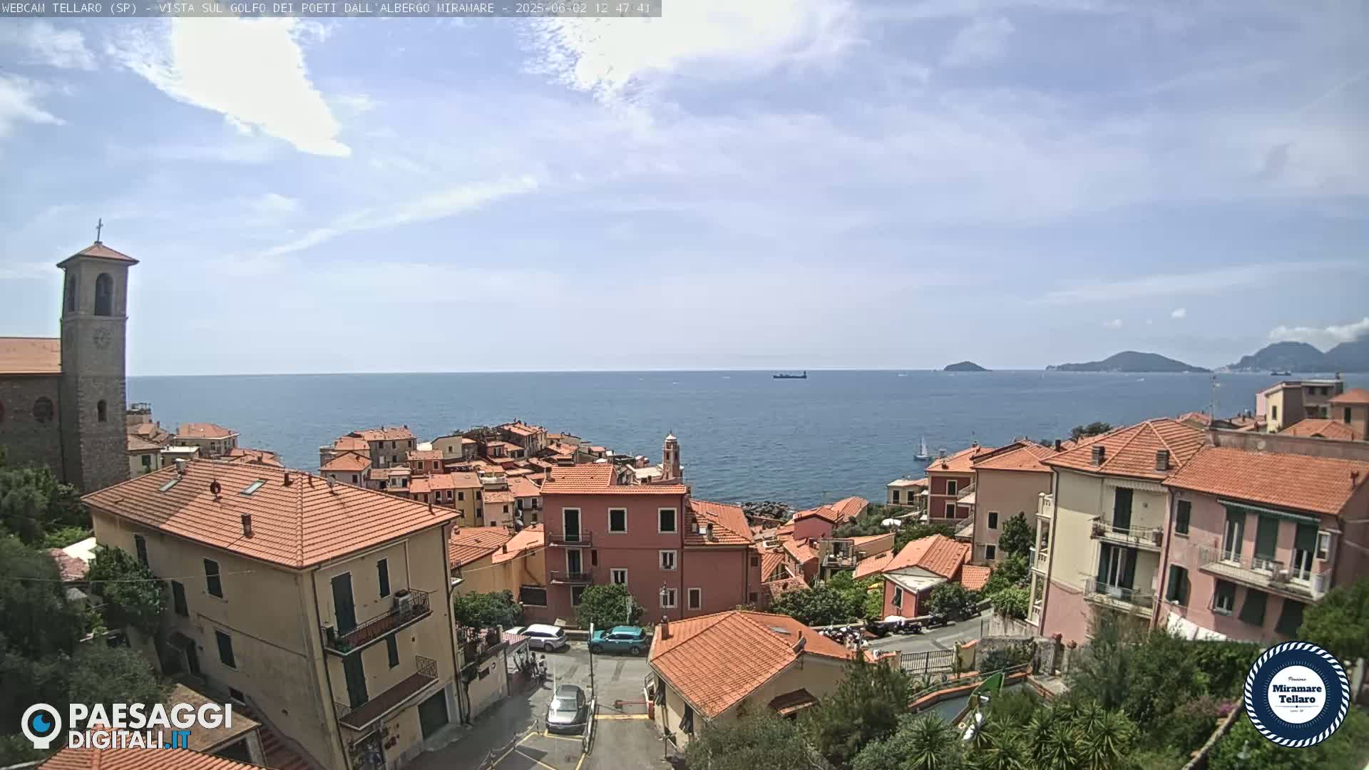 A coastal town with red-tiled roofs overlooks a calm ocean under a partly cloudy sky.