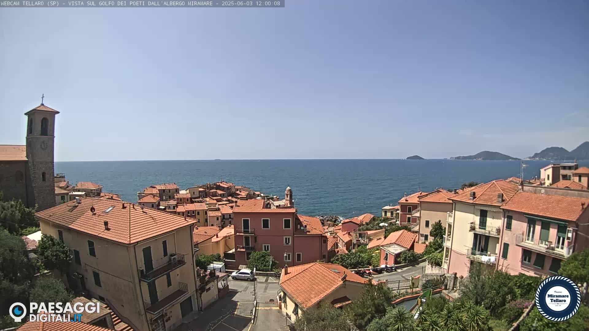 A coastal town with red-tiled roofs overlooks a calm blue sea under a clear sky.