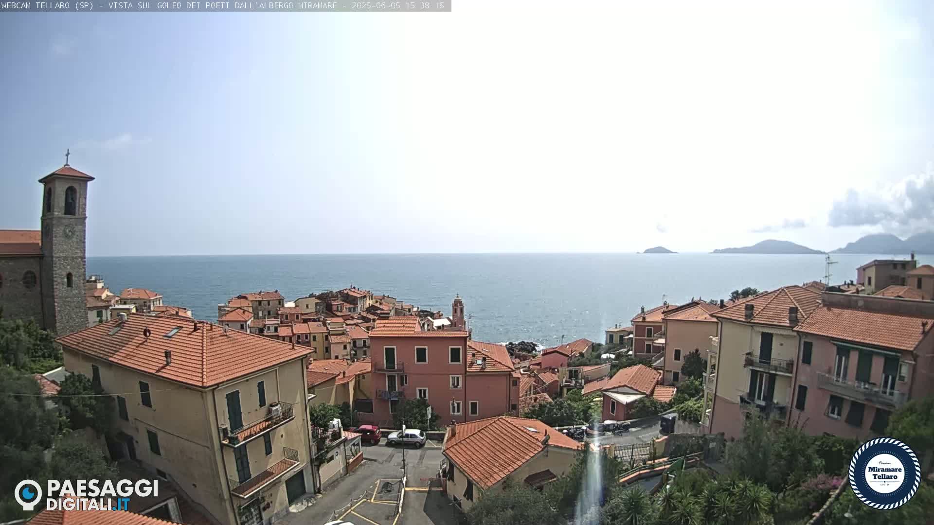 A coastal town with red-tiled roofs overlooks a calm sea under a mostly clear sky.