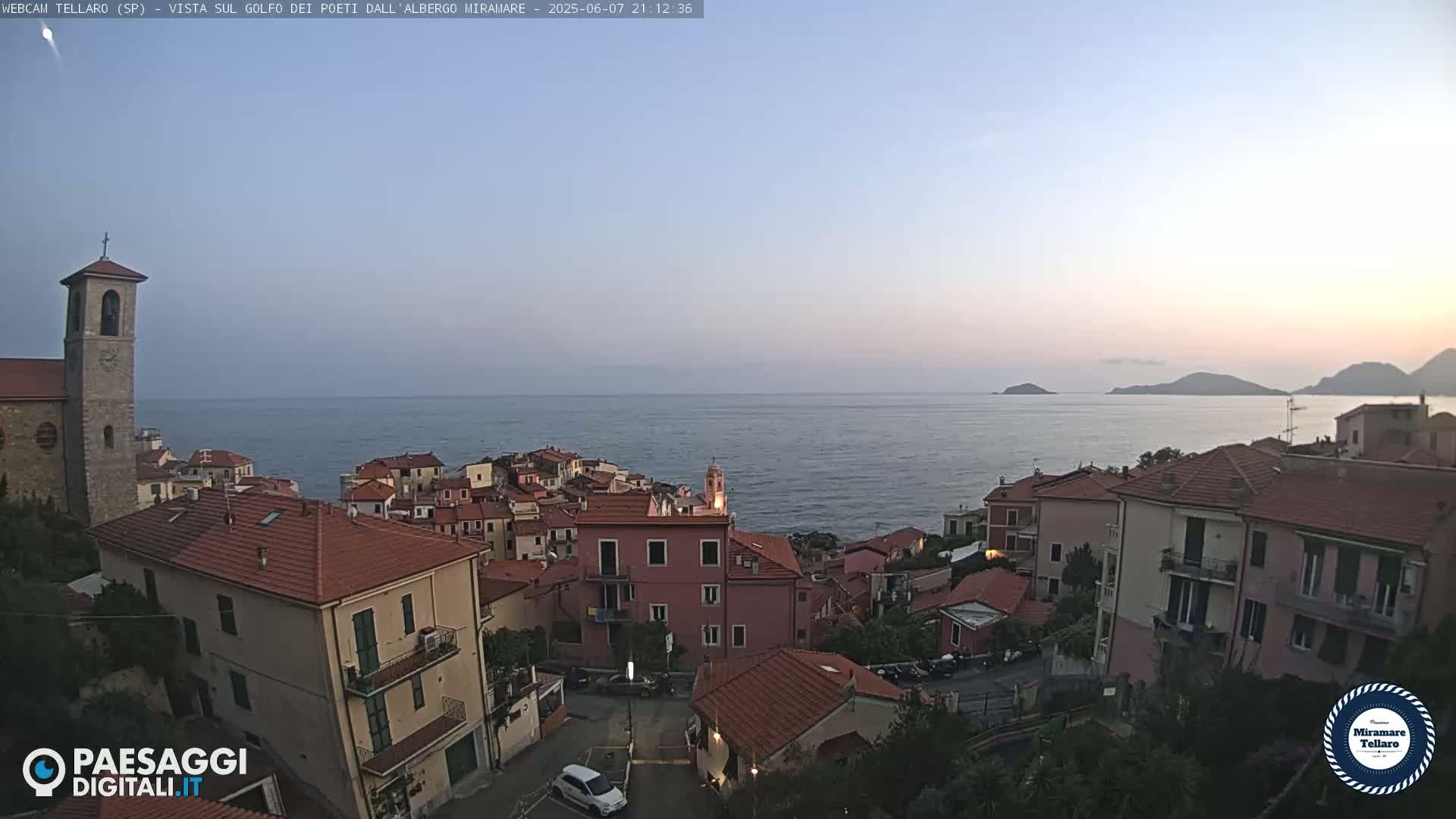 A coastal town with red-tiled rooftops overlooks a calm sea under a twilight sky.