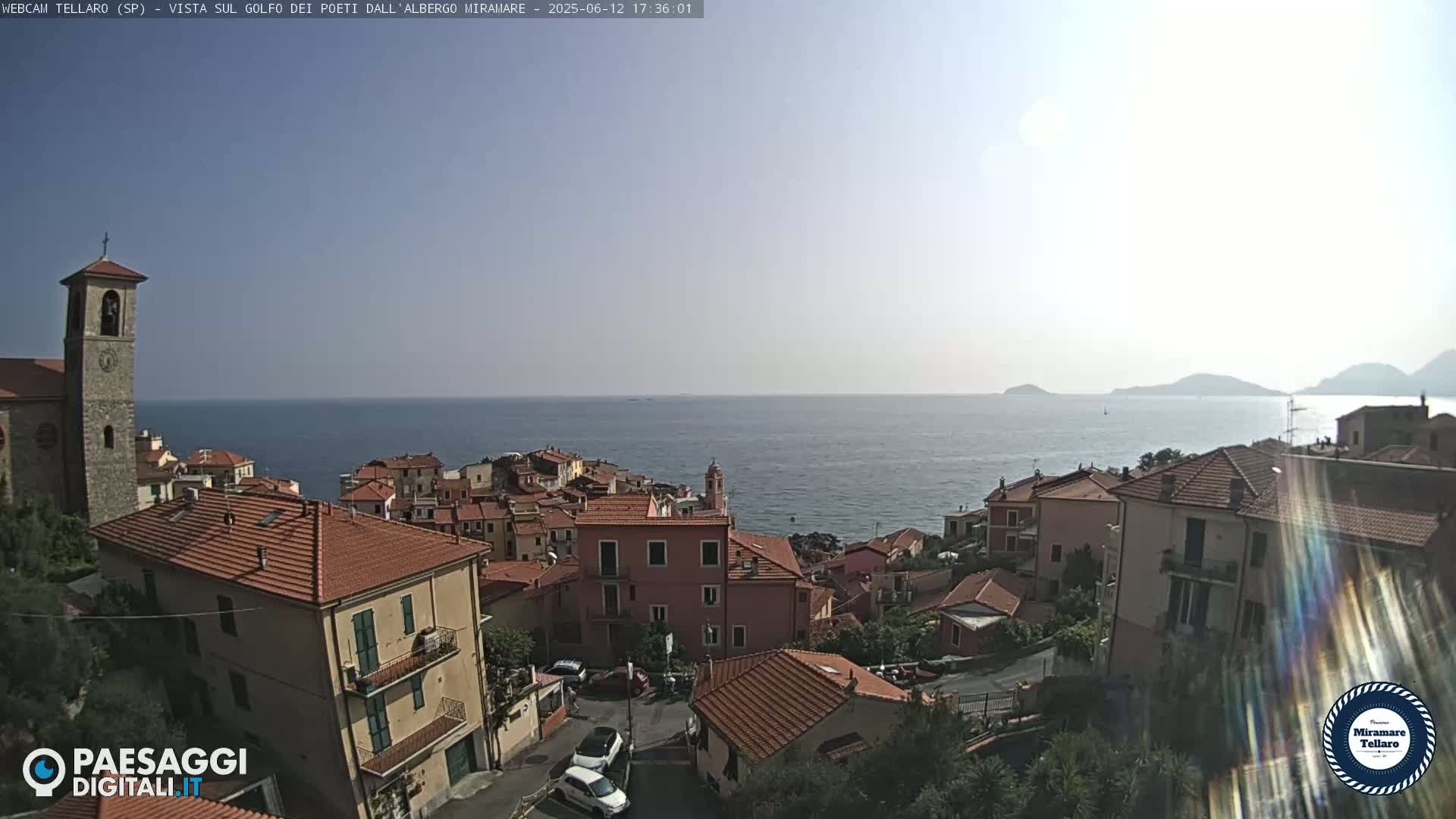 A coastal town with red-tiled roofs overlooks a calm sea under a clear, sunny sky.