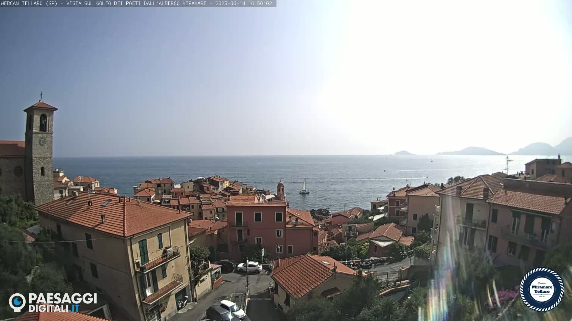 A coastal town with red-tiled roofs overlooks a calm sea on a sunny day.