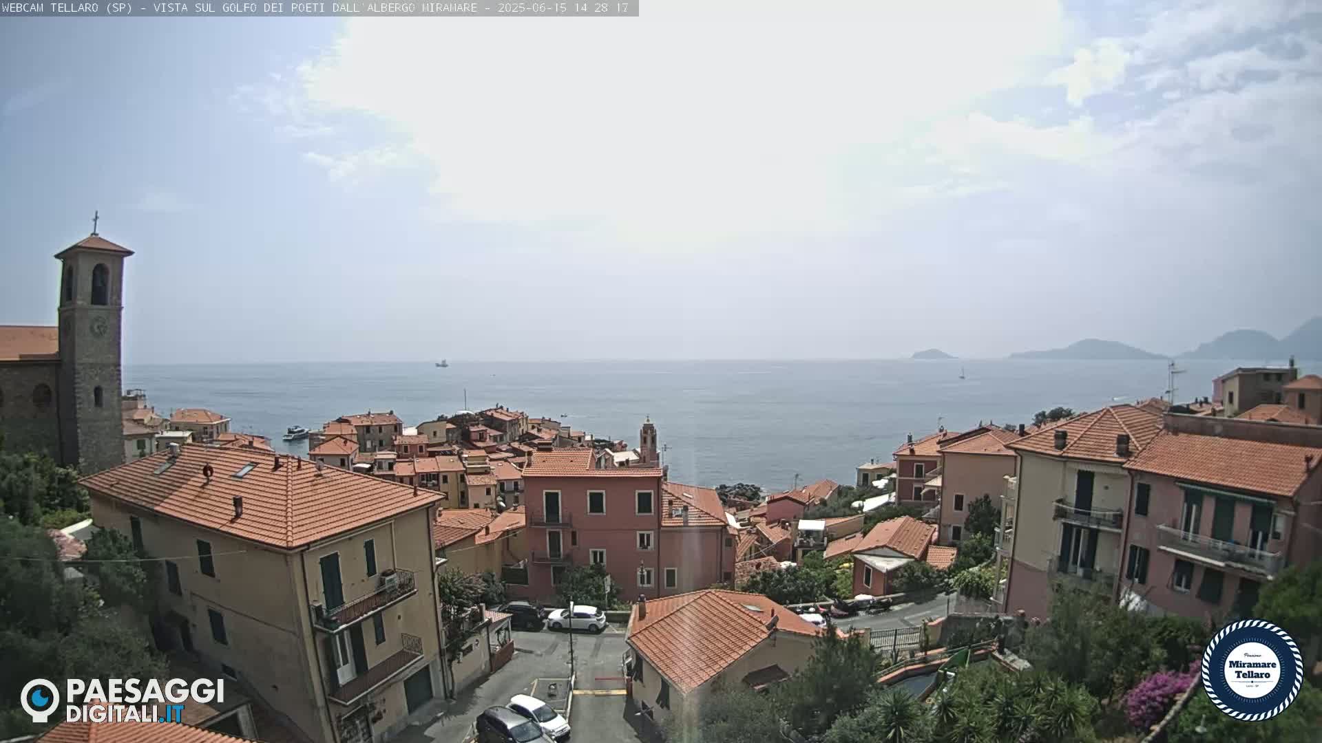 A coastal town with red-tiled roofs overlooks a calm sea under a hazy sky.