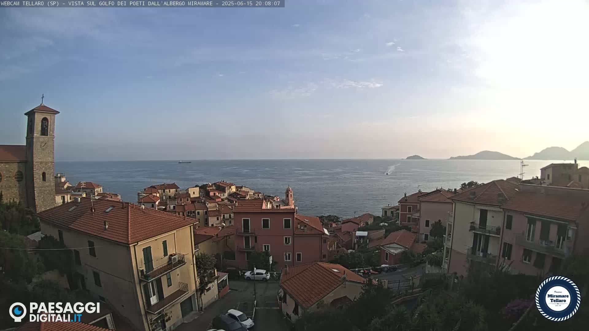A coastal town with red-tiled roofs overlooks a calm sea under a mostly clear sky.