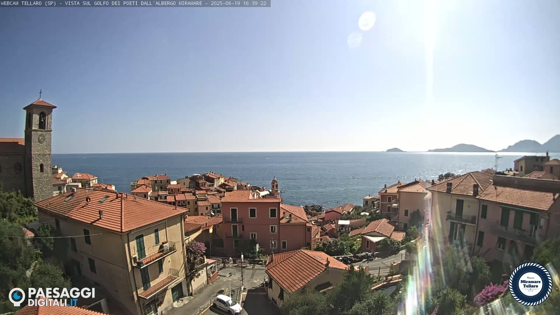 A coastal town with red-tiled roofs overlooks a calm blue sea under a sunny sky.