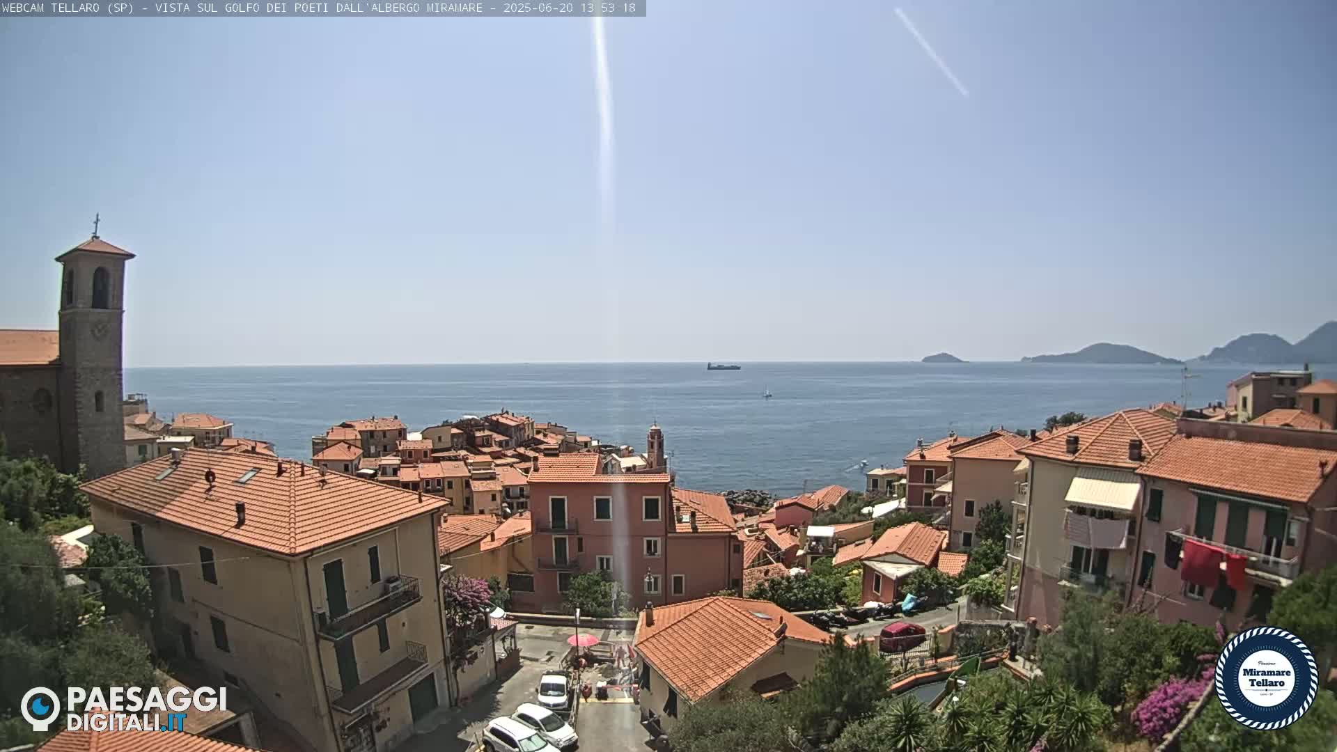 A coastal town with red-tiled roofs overlooks a calm blue sea under a clear, sunny sky.