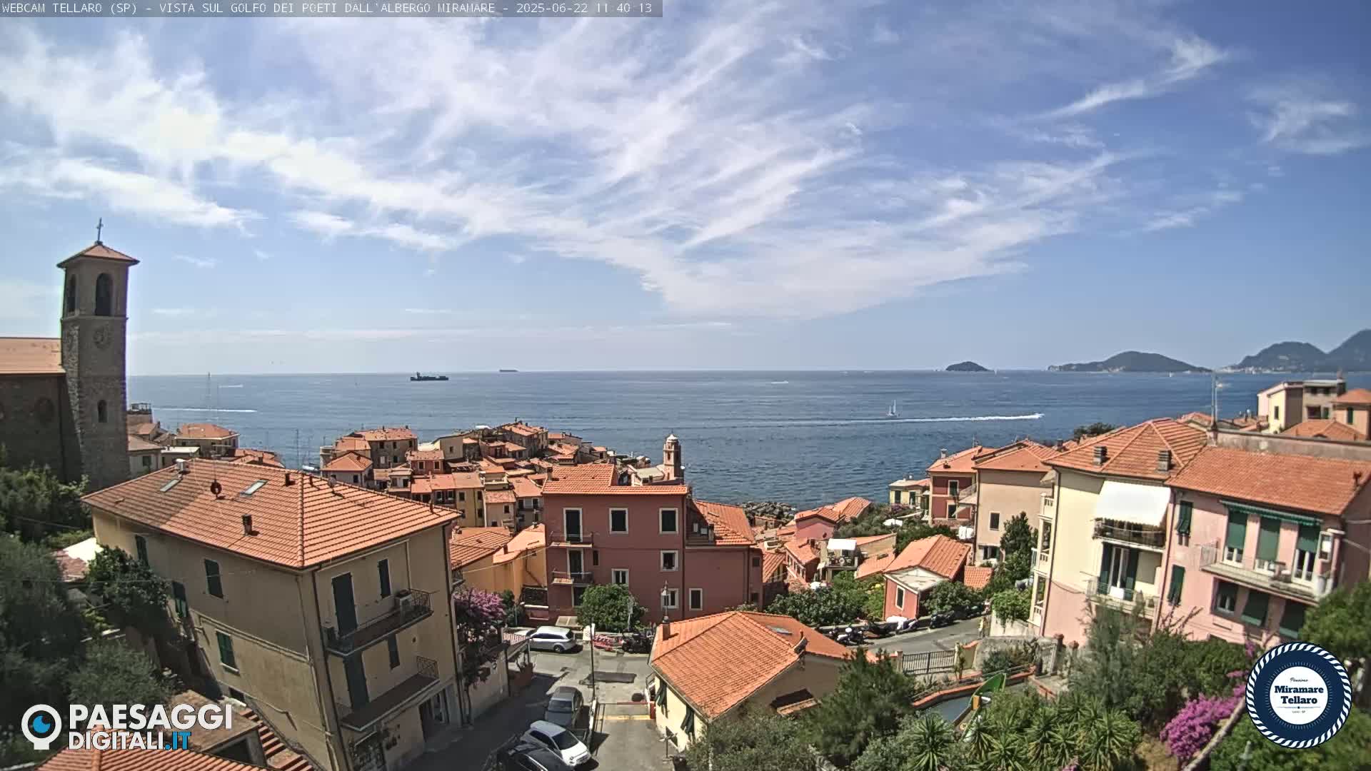 A coastal town with red-tiled roofs overlooks a calm sea under a partly cloudy sky.