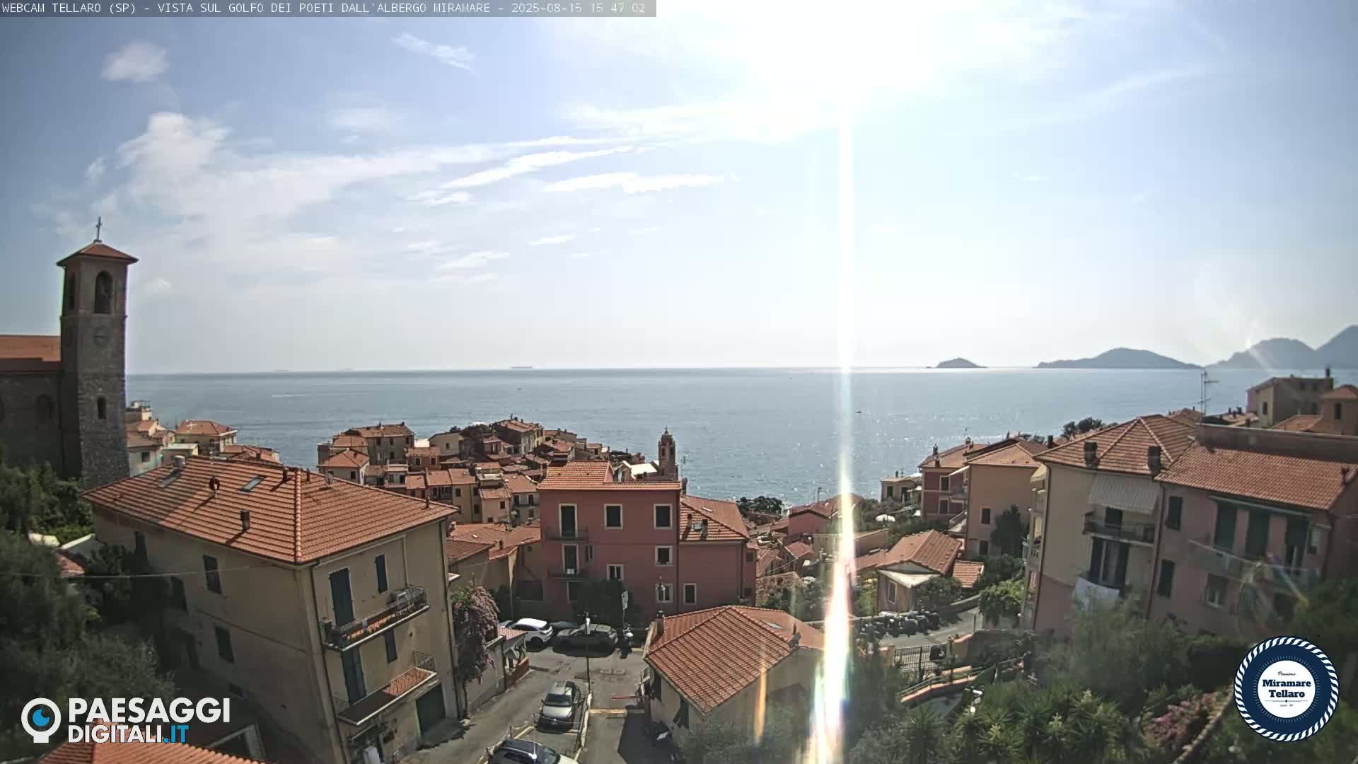 A coastal town with red-tiled roofs overlooks a calm blue sea under a mostly clear sky.