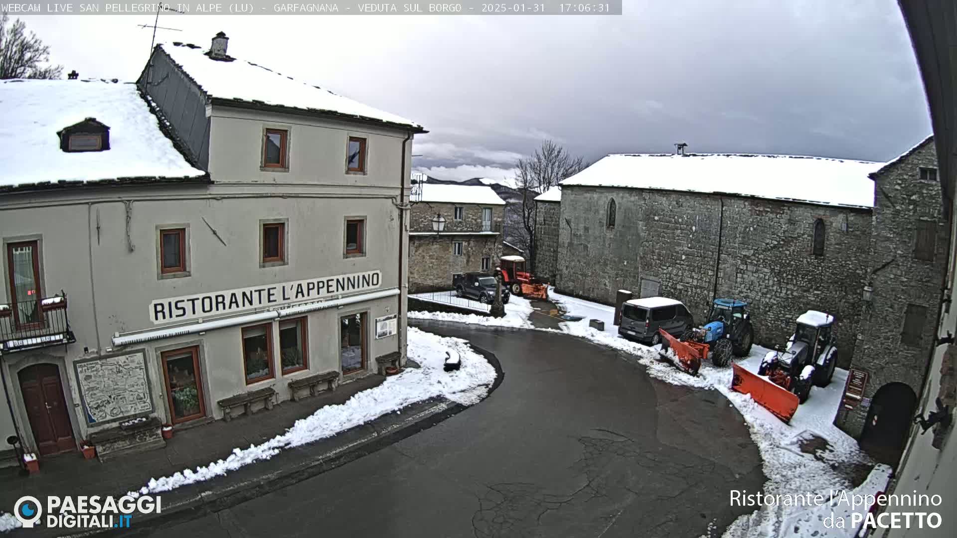 A snow-covered village square with several buildings, including a restaurant, and snow-clearing equipment.