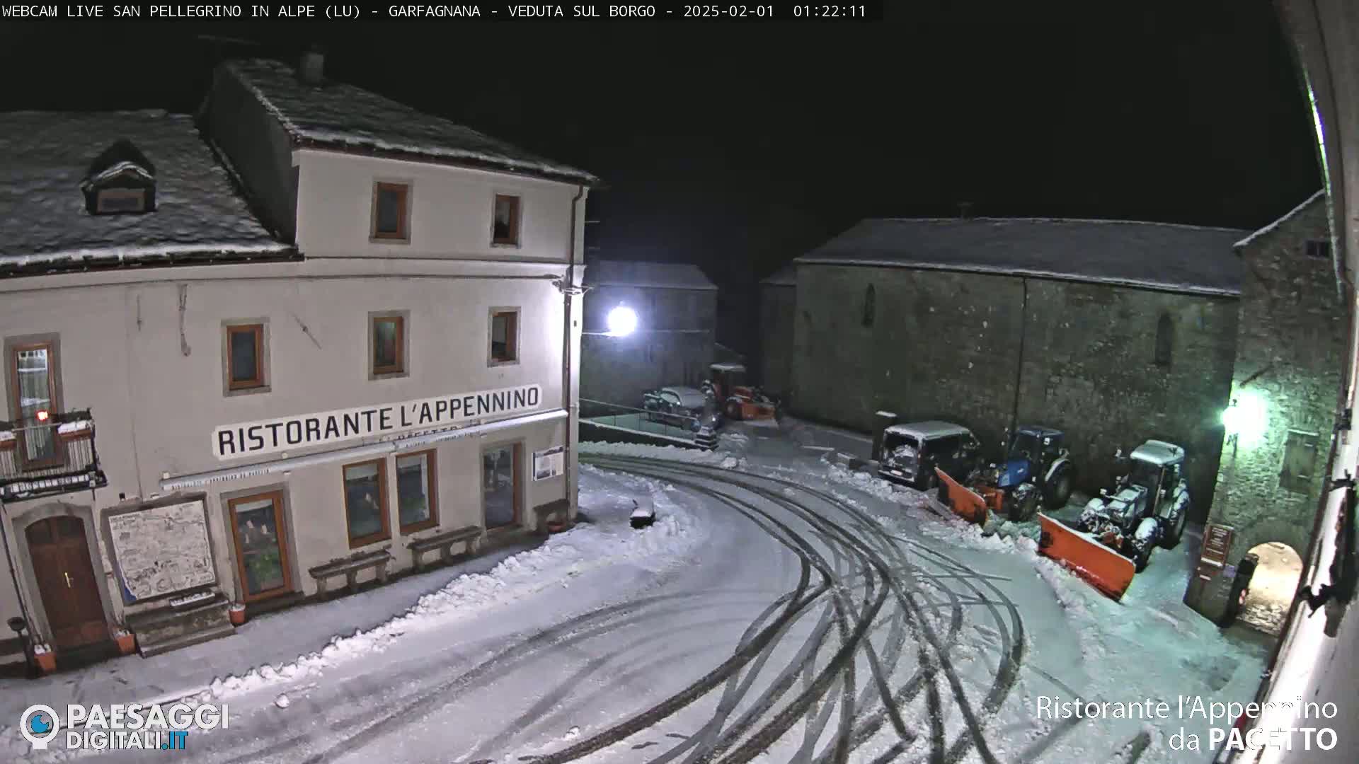 A snow-covered town square at night, with several parked vehicles and snowplows, features a restaurant called "Ristorante L'Appennino."