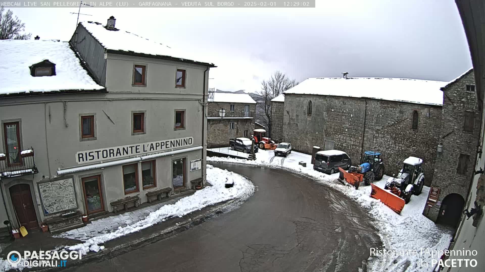 A snow-covered village square with several parked cars and snow plows, and a restaurant called "Ristorante L'Appennino".