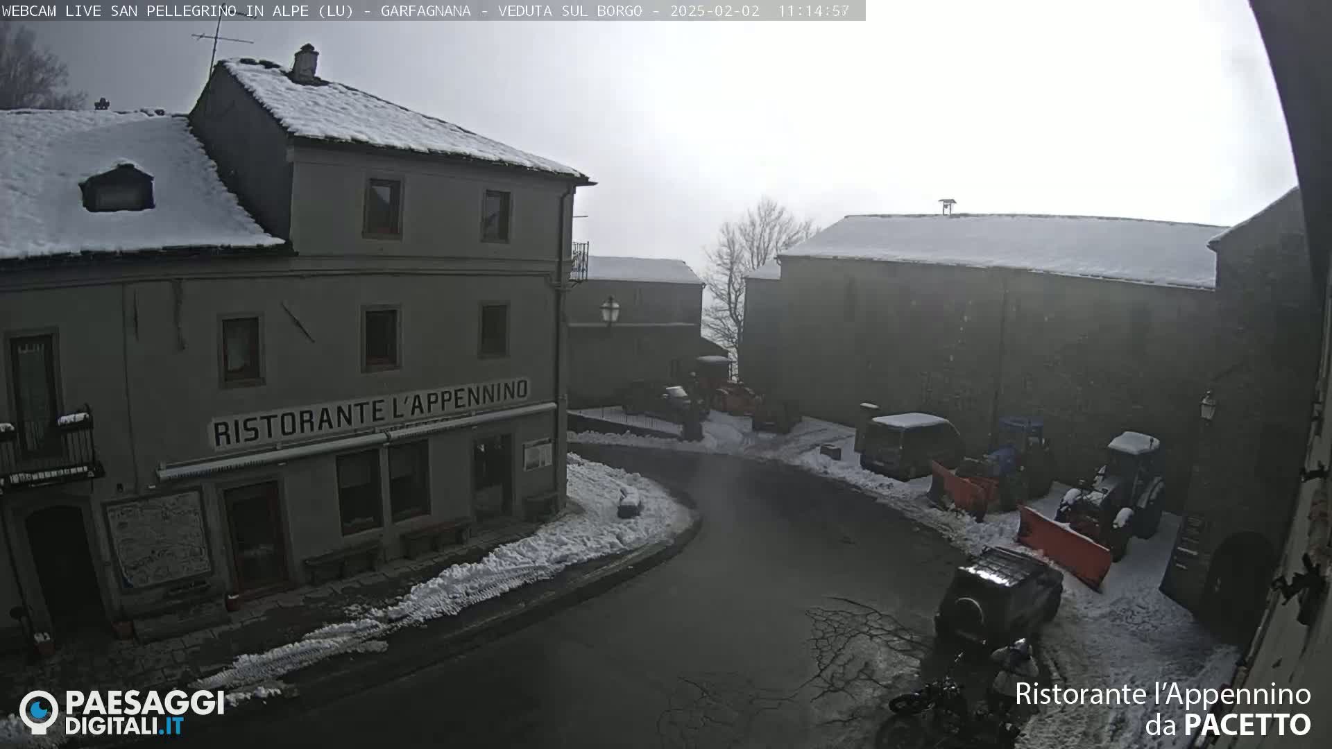 Snow-covered buildings and vehicles are visible in a town square during a light snowfall.