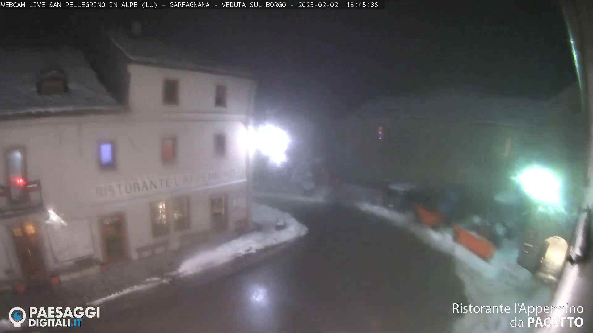 A nighttime, snowy scene shows a restaurant and a street, illuminated by streetlights.