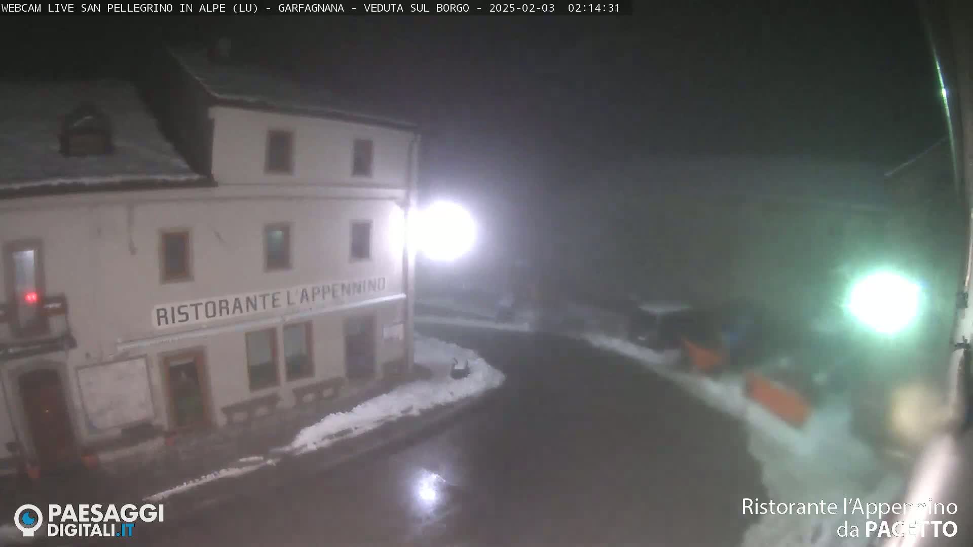 A nighttime view of a restaurant, partially covered in snow, during a snowfall.