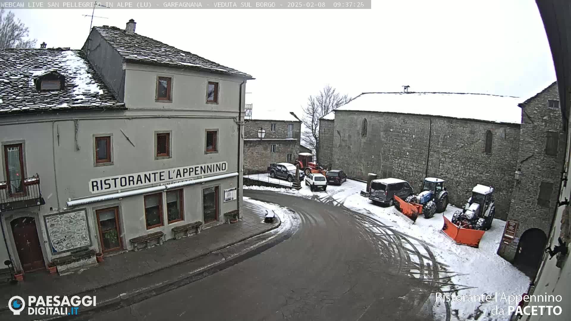 A snow-covered village square with several parked cars and snowplows, featuring a restaurant called "Ristorante L'Appennino".