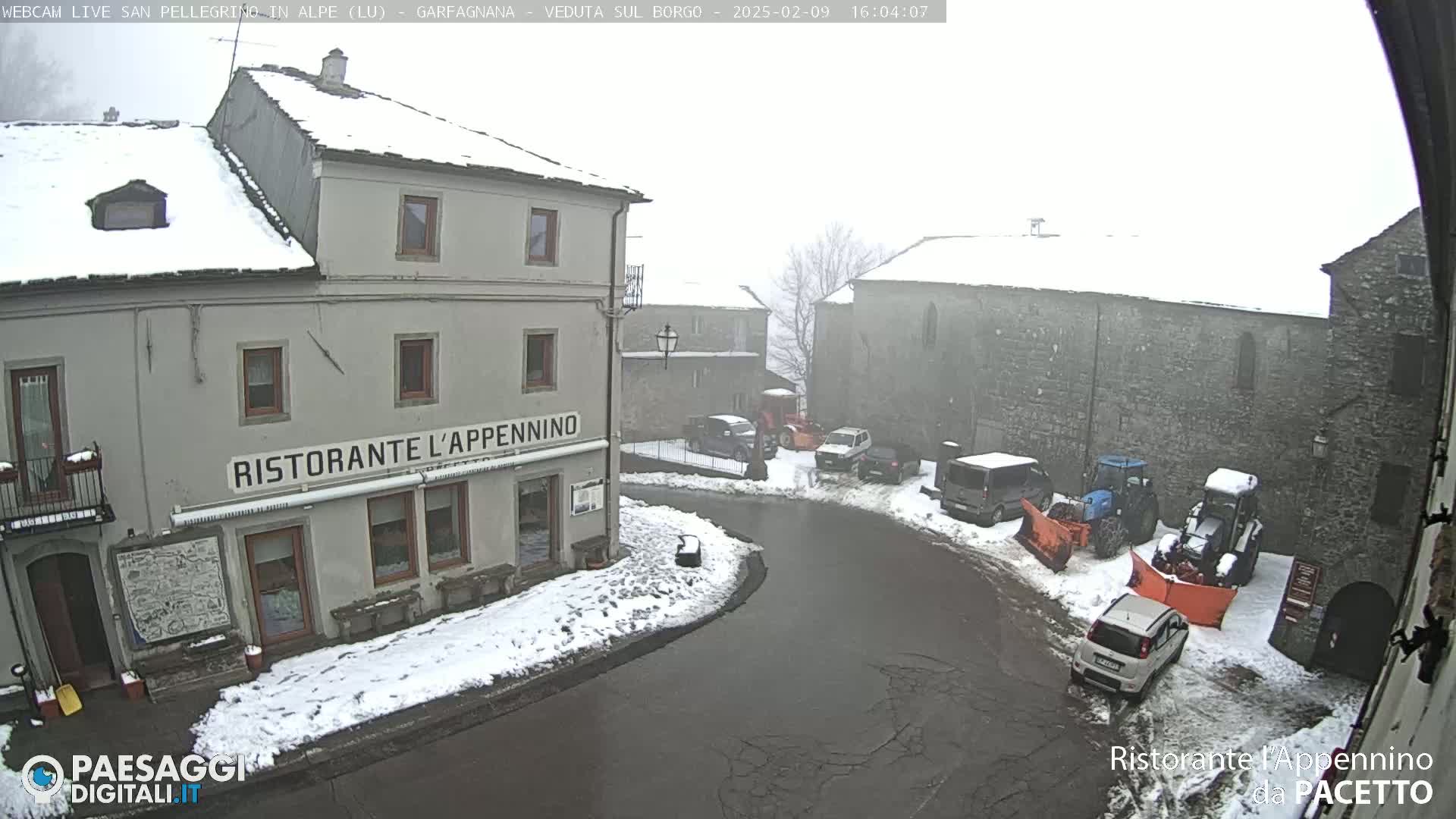 A snow-covered village square with several cars and snow-clearing equipment, and a restaurant called "Ristorante L'Appennino".