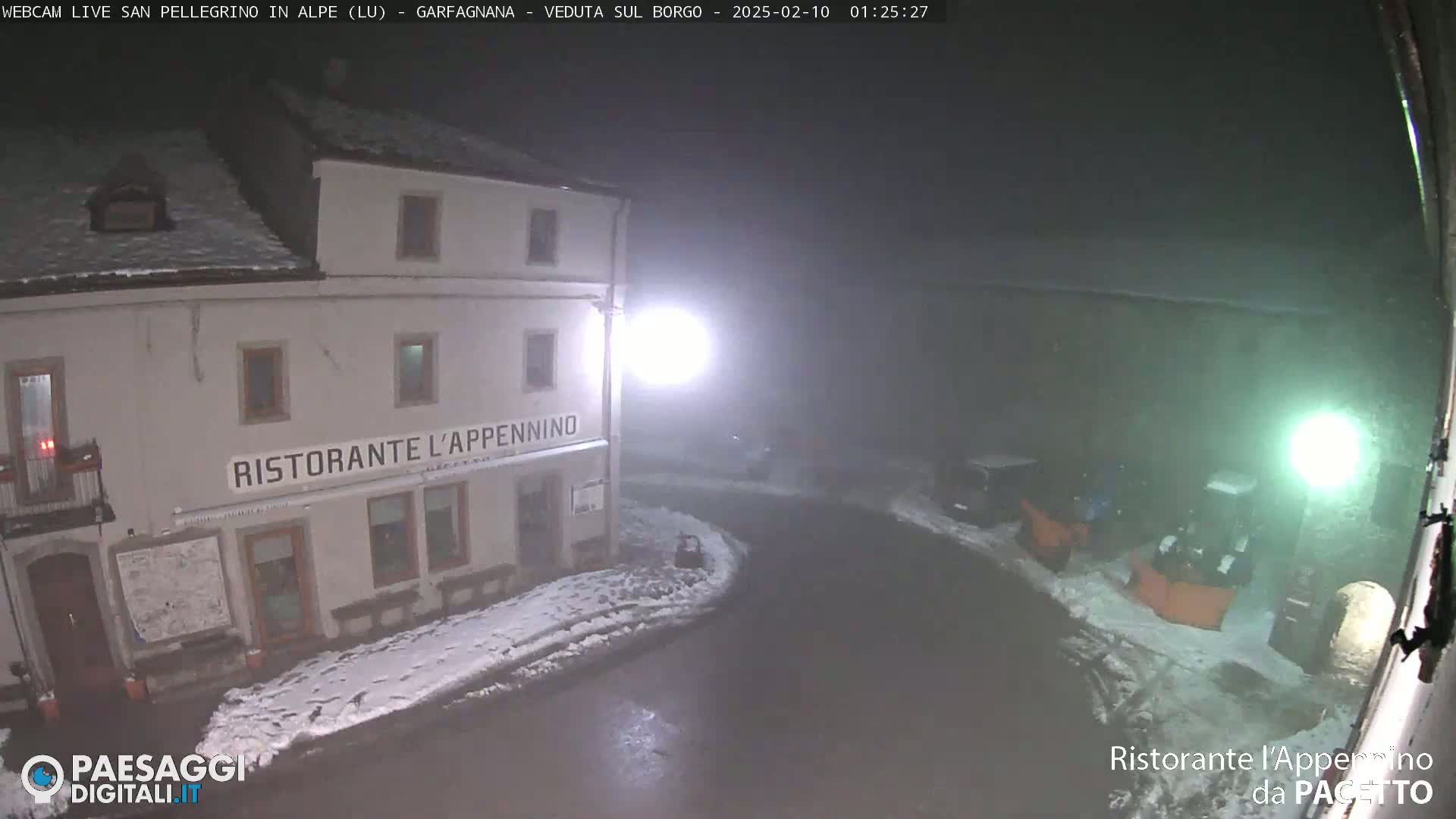 A snow-covered nighttime street scene shows a restaurant called Ristorante L'Appennino, illuminated by streetlights, with some vehicles parked nearby in foggy conditions.