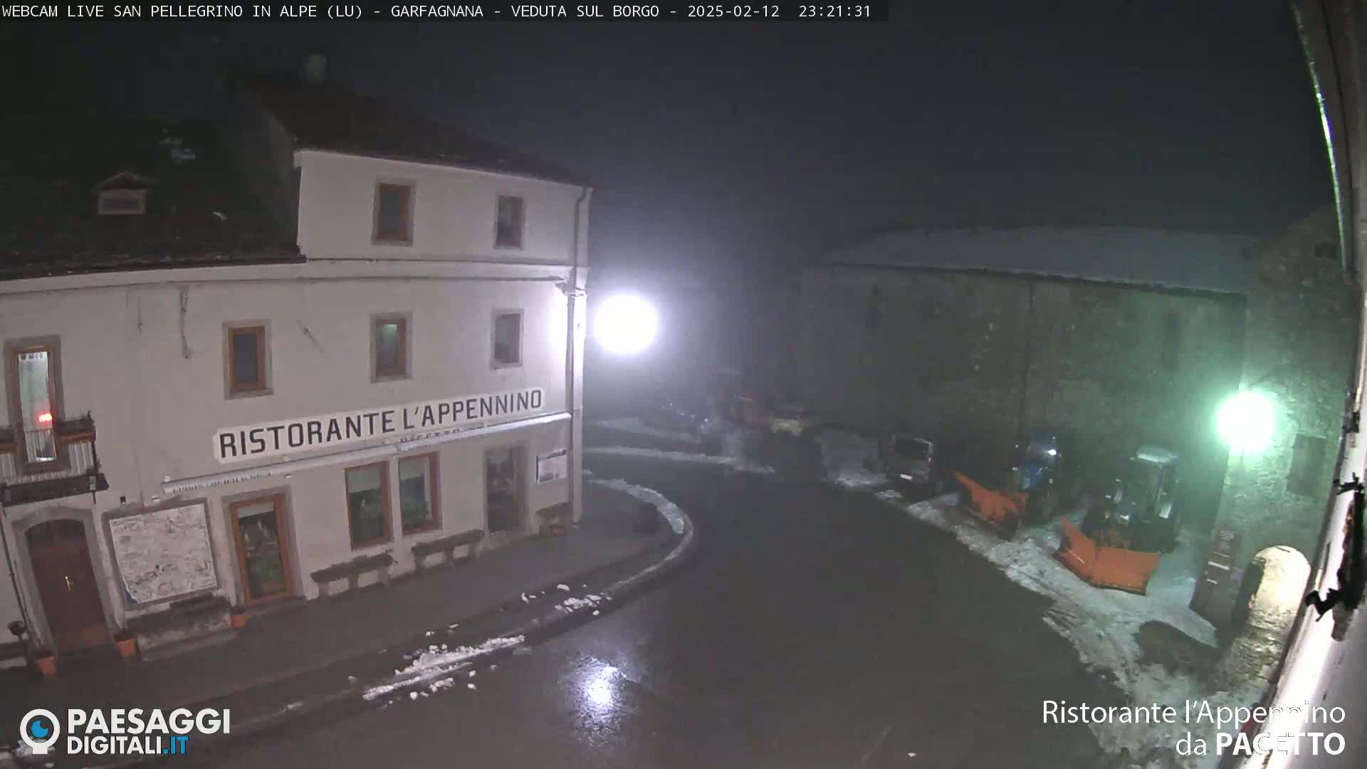 A nighttime, snowy scene shows a restaurant called Ristorante L'Appennino and a street with parked cars and snowplows.